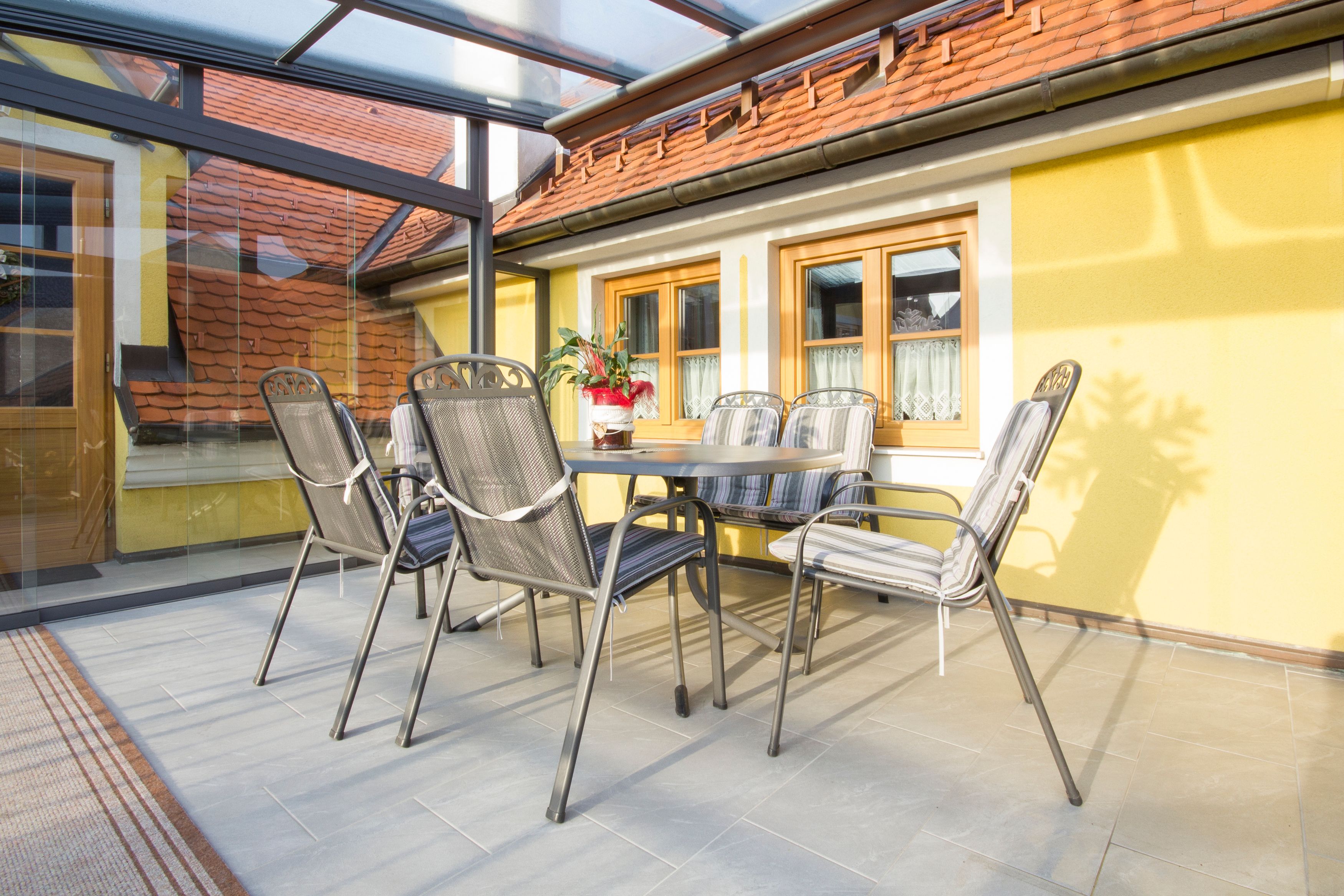 Winter garden with table and chairs, yellow walls, glass roof.