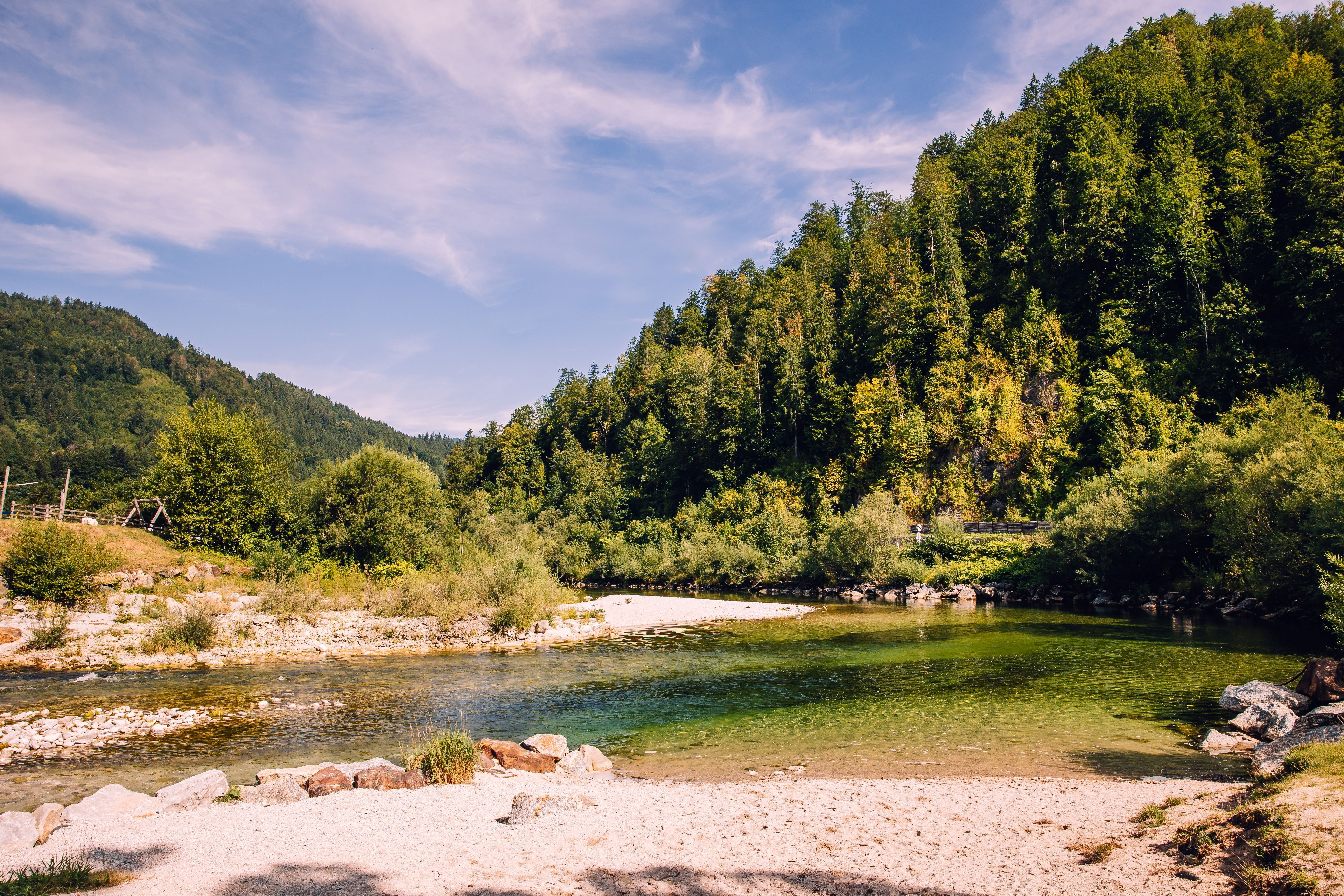 Landscape near Göstling: a clear river with a gravel bank, surrounded by wooded slopes under a blue sky.
