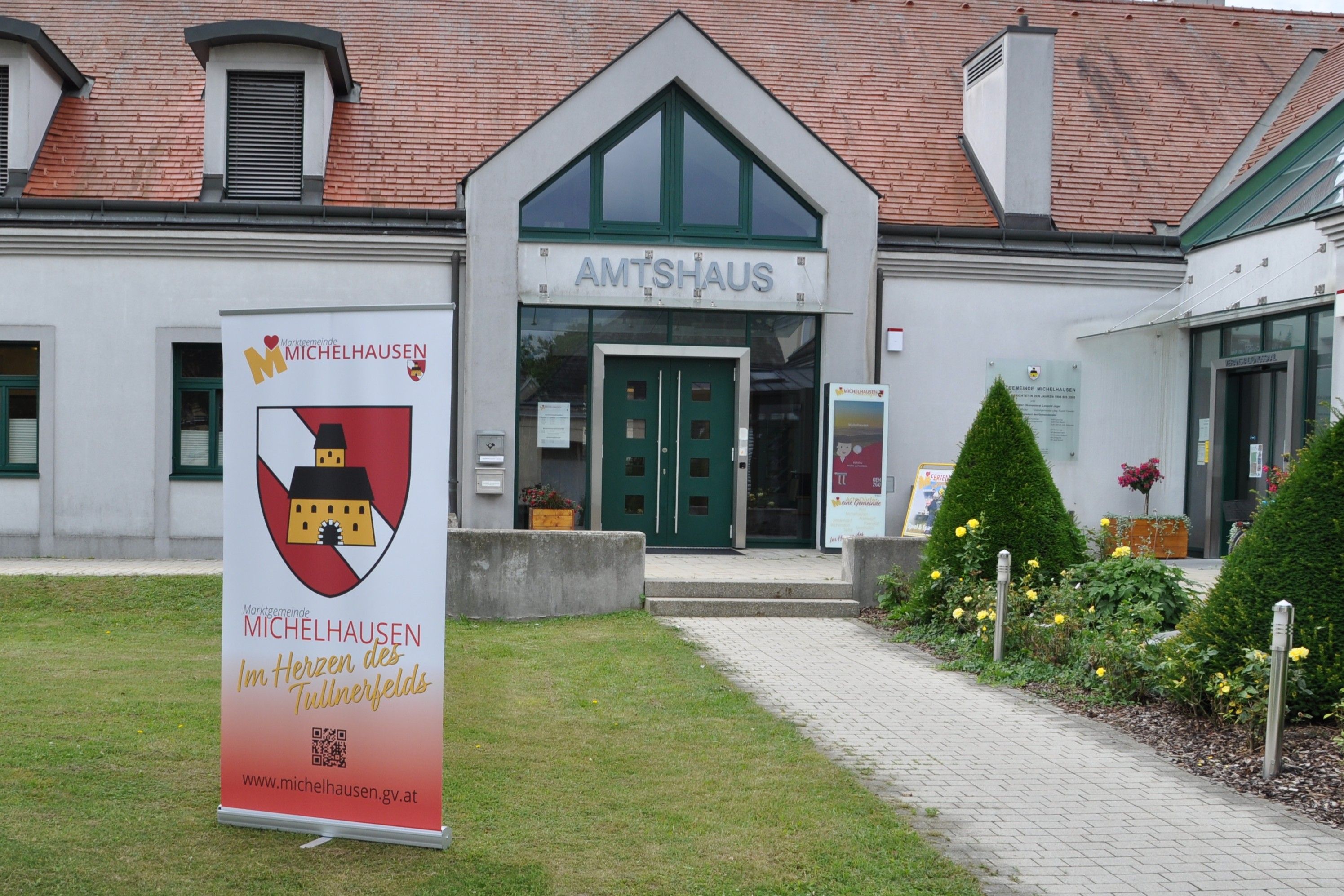 Entrance to the Amtshaus Michelhausen with advertising banner and well-tended garden.