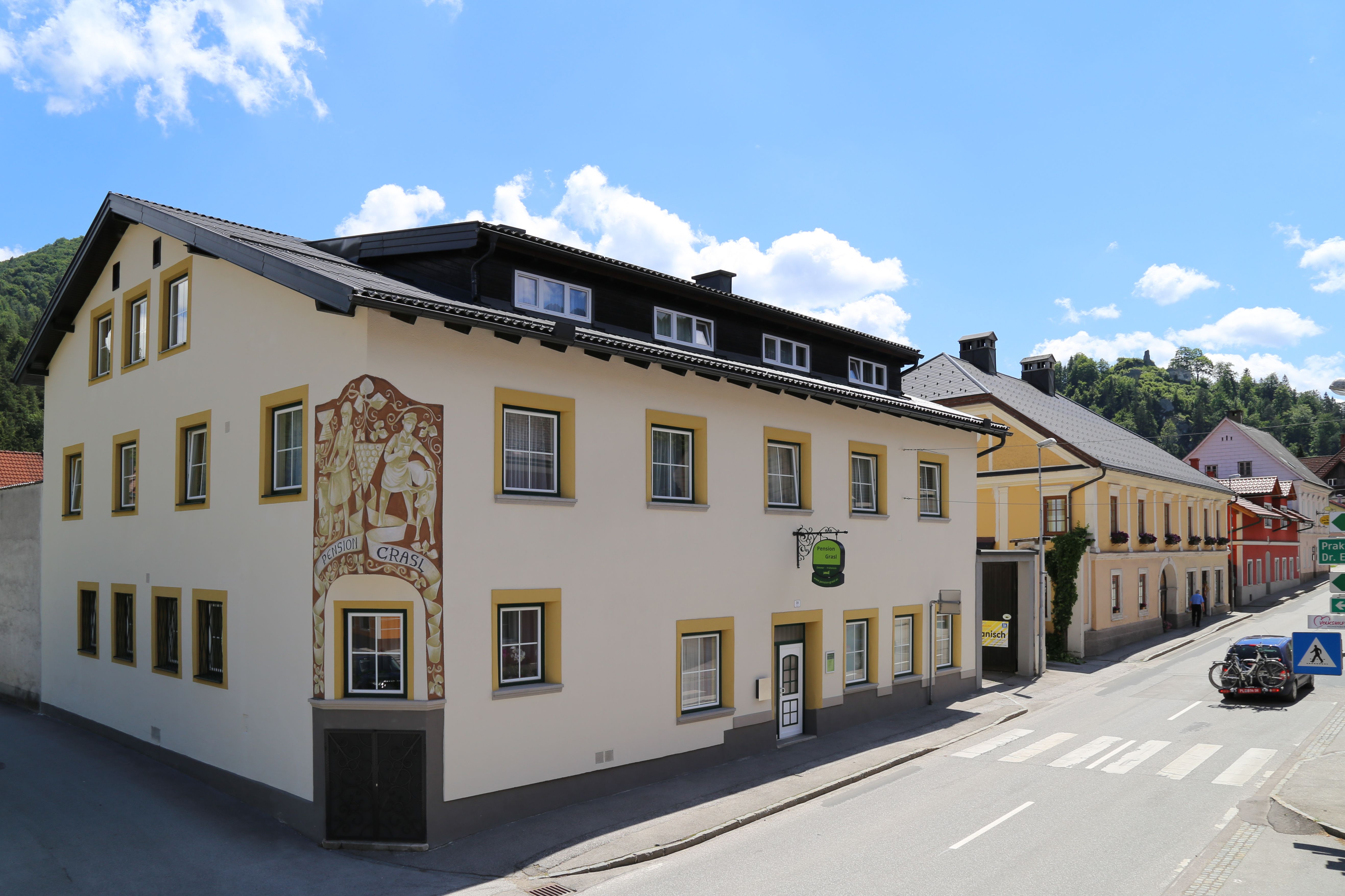 A yellow building with the sign 'Pension Grasl' on a street in sunny weather.