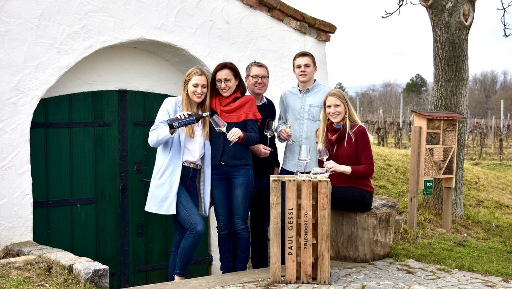 A family stands in front of an outdoor wine cellar, with wine glasses and a bottle of wine.