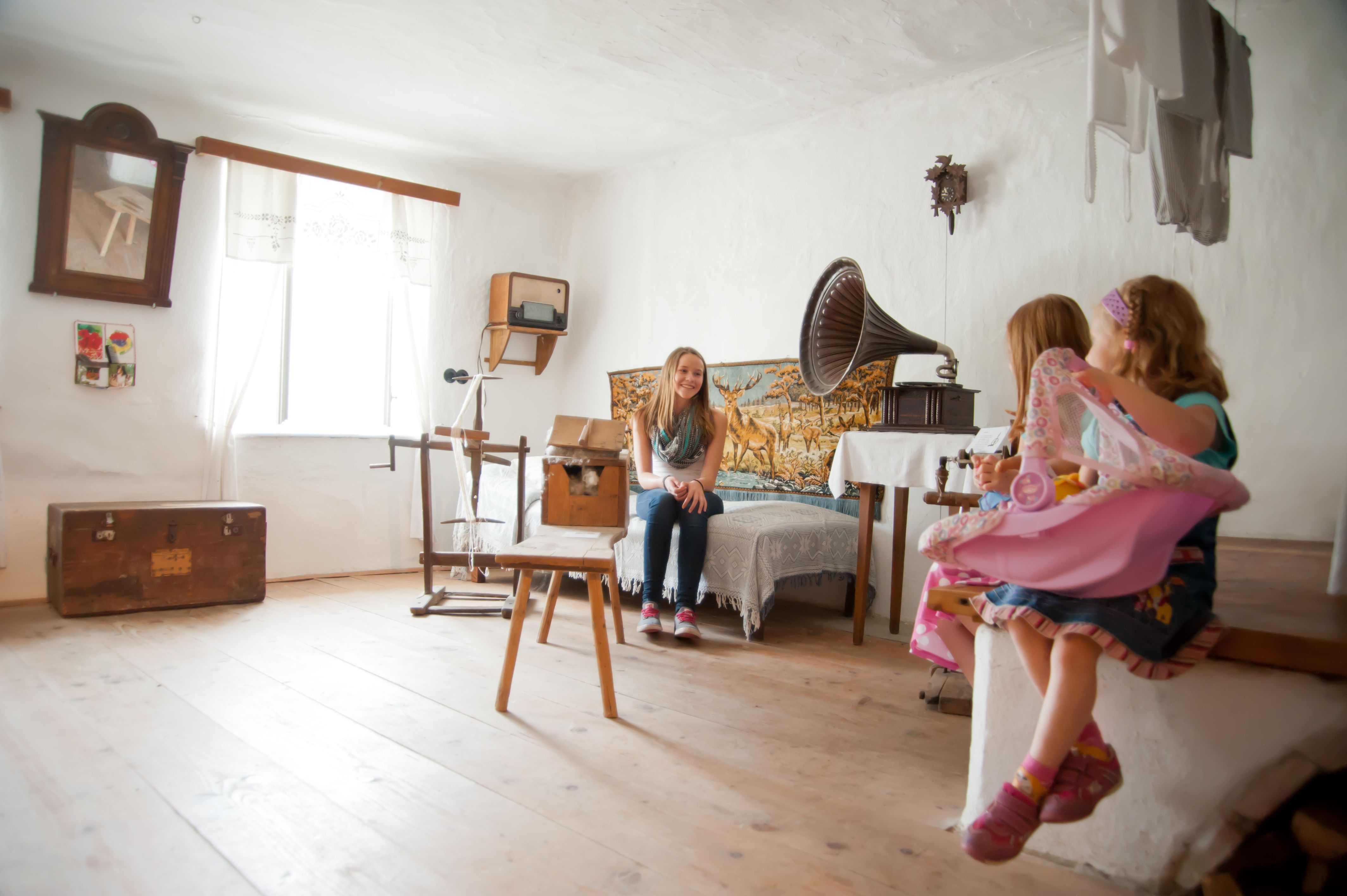 A room in the Langau Leisure Museum with antique furniture and a gramophone. Two children are sitting on a bench, a girl is sitting on a bed.