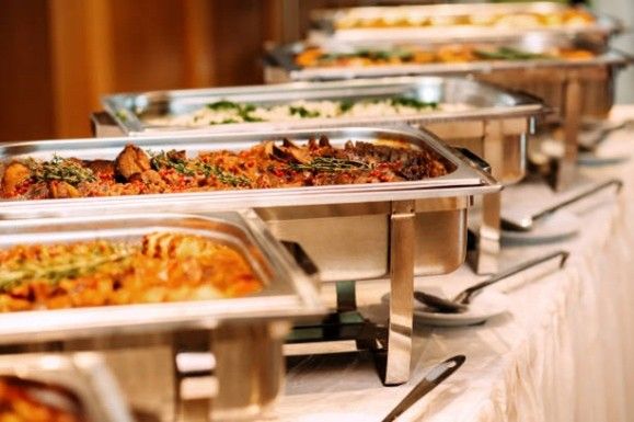 A buffet with several stainless-steel serving containers filled with food on a set table.