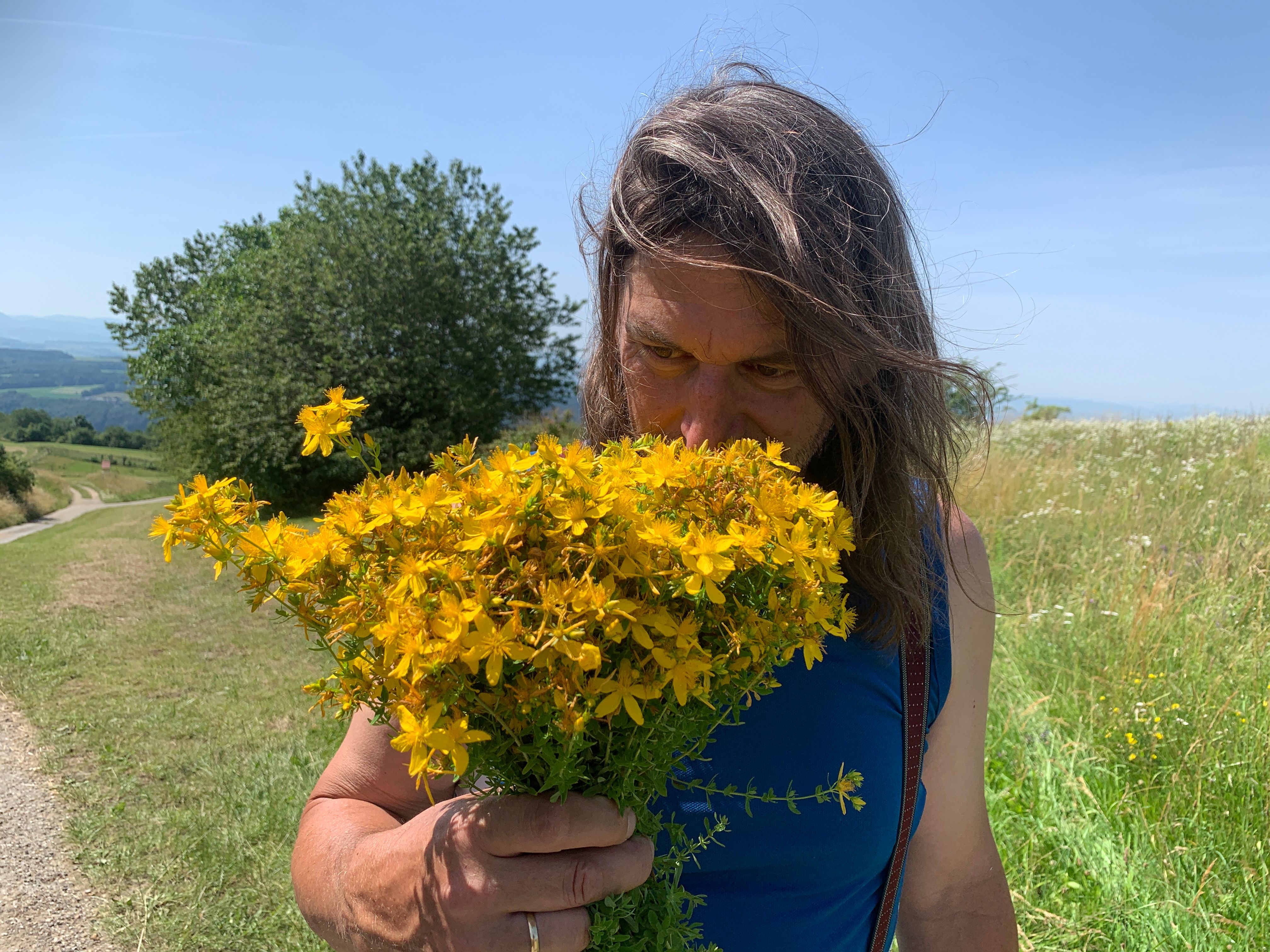 A person smells a bunch of yellow flowers on a country lane.