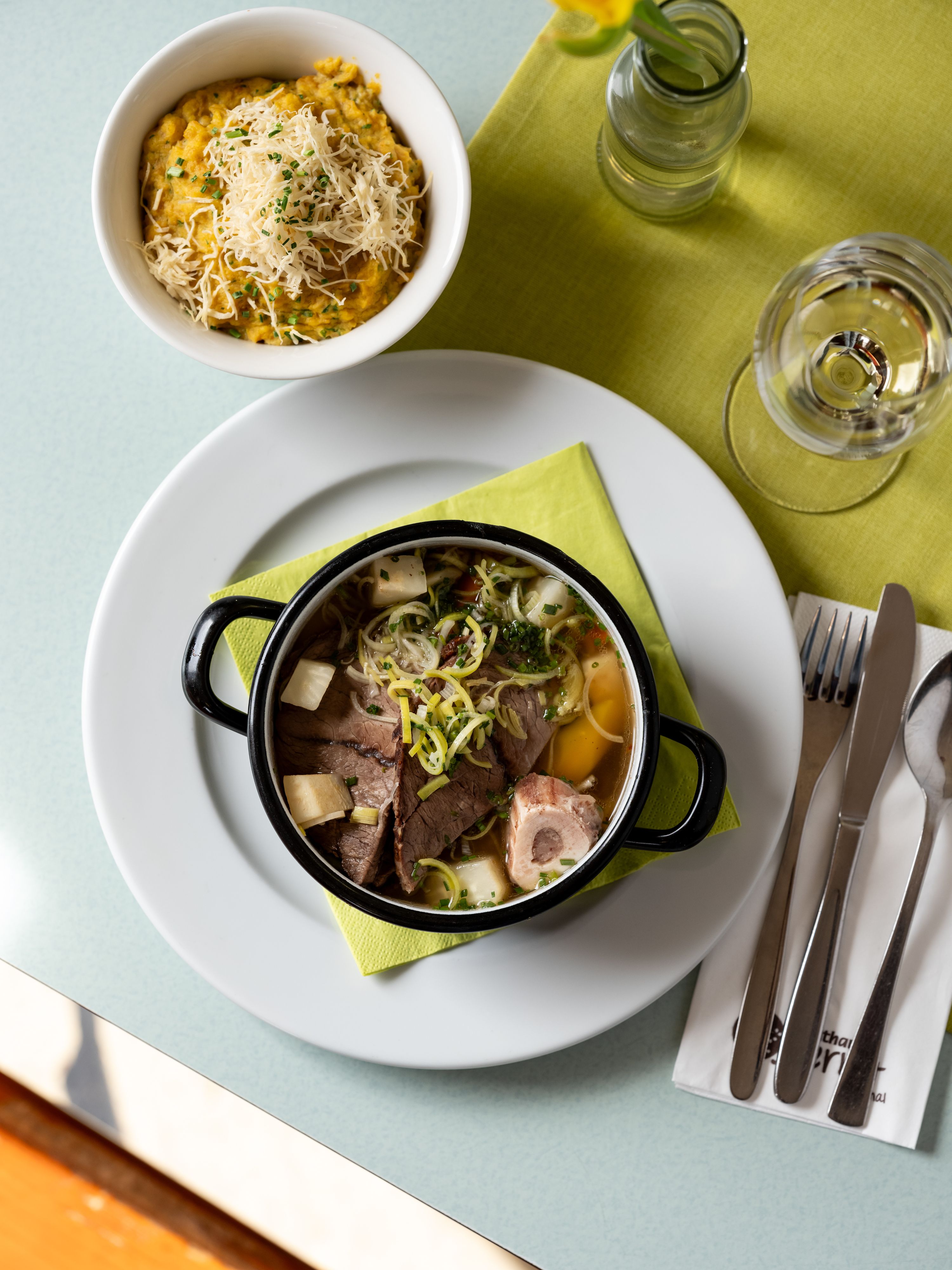 A table with a plate of soup, a bowl of porridge with cheese, a glass of water and cutlery on a green napkin.