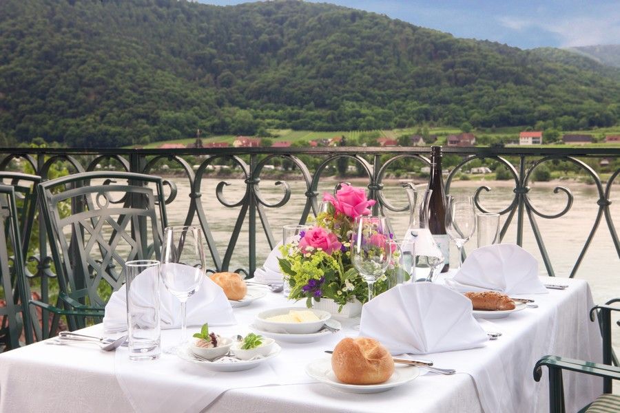 Set table on a terrace with a view of the Danube and wooded hills in the background.