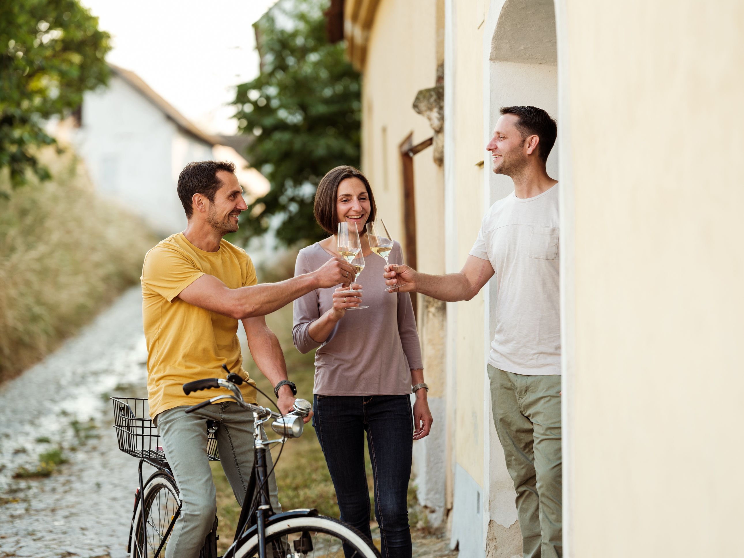 Three people clink glasses of wine, one person sits on a bicycle.