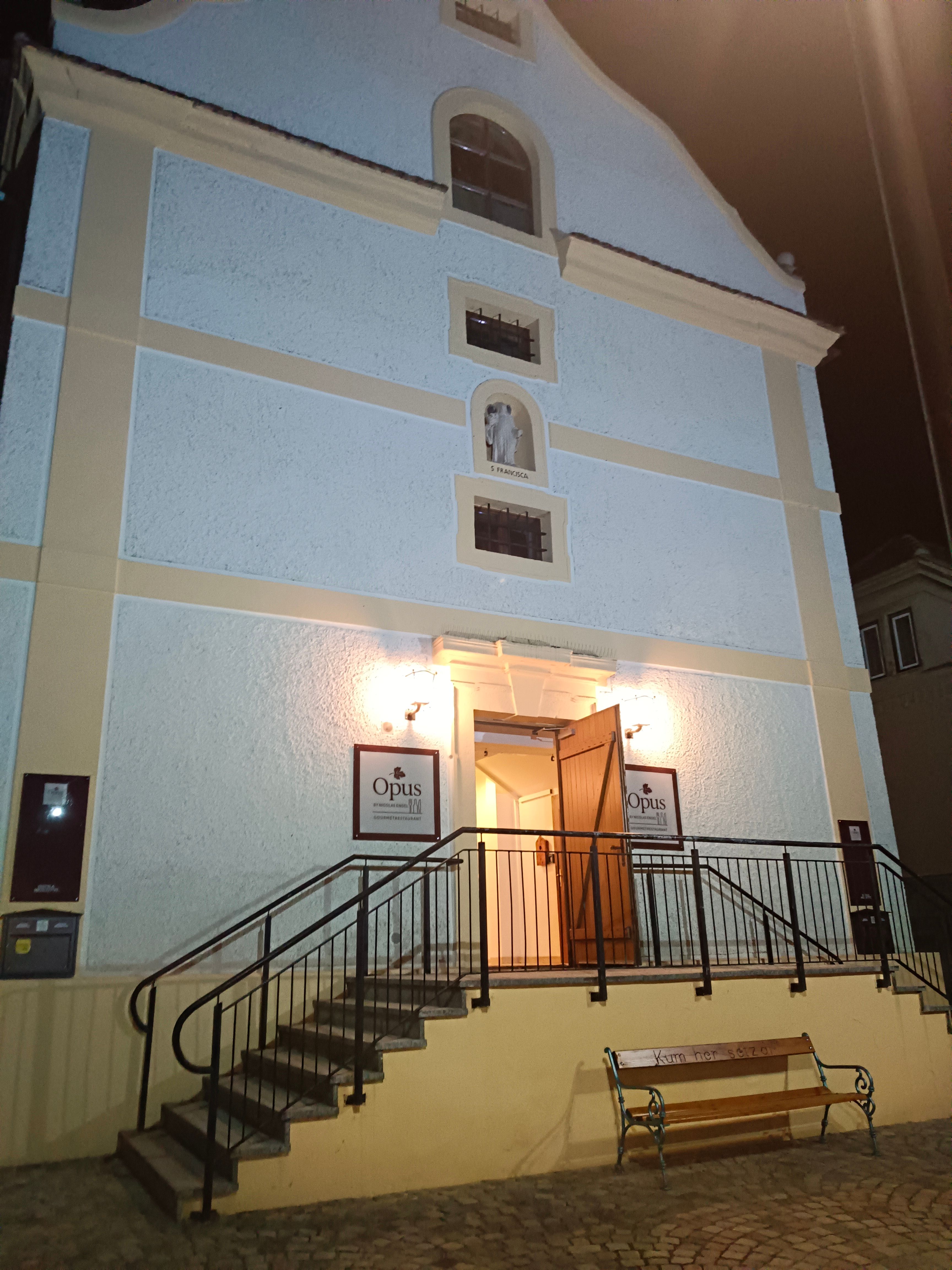 Entrance of a building with stairs and open doors, illuminated at night.