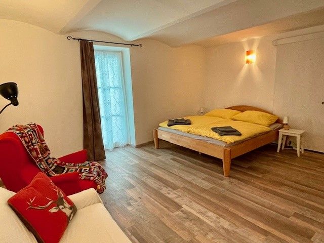 Cozy bedroom with wooden floor, double bed, red armchair and window with curtain.