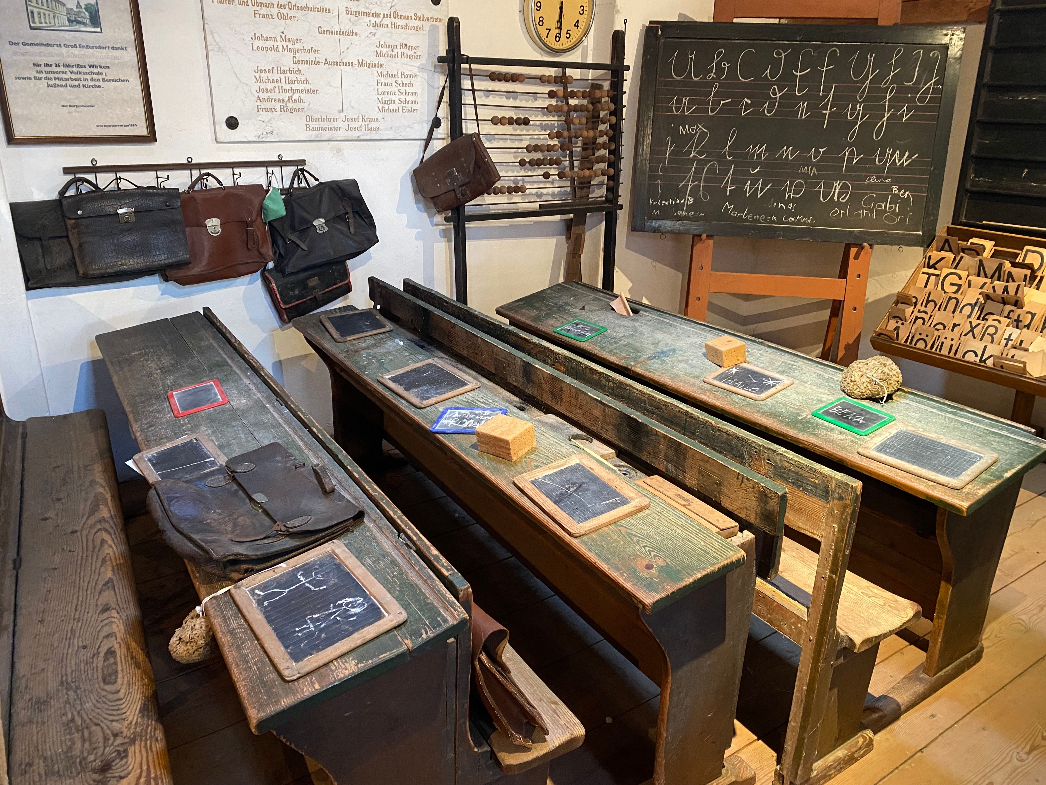 Historic classroom with old wooden benches, slates and a blackboard with writing exercises.