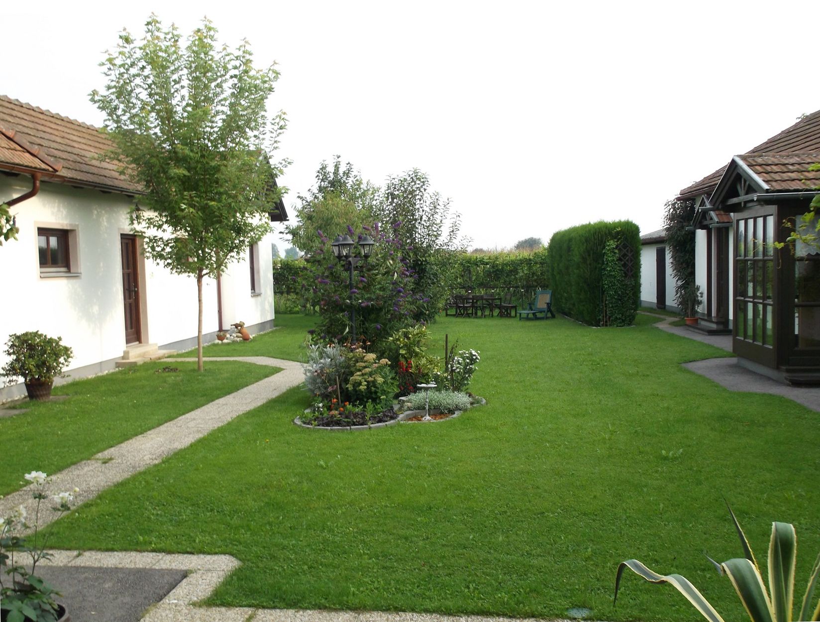 Very well-kept garden with a view of shrubs and trees, with part of the building in the background.