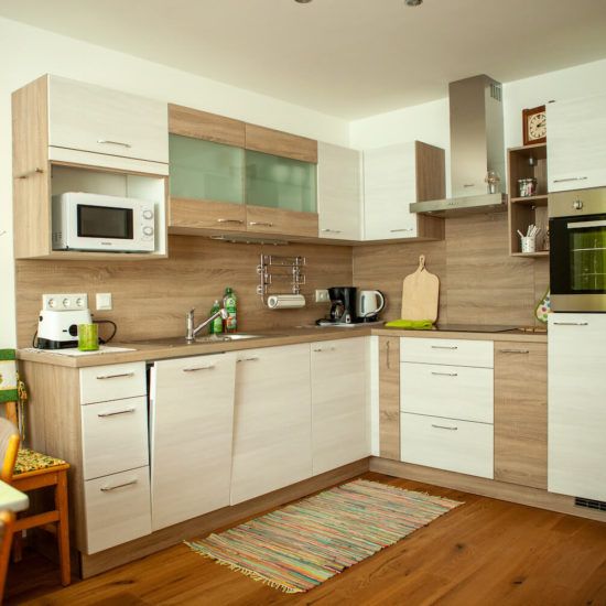Modern kitchen with wooden and white cupboards, microwave, coffee machine and oven.