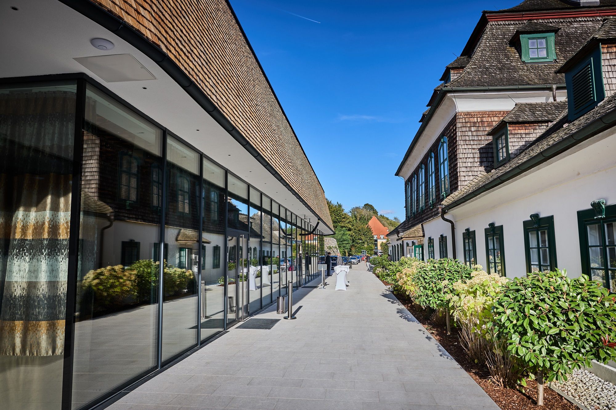 Modern glass façade next to historic building with green window frames, blue sky.