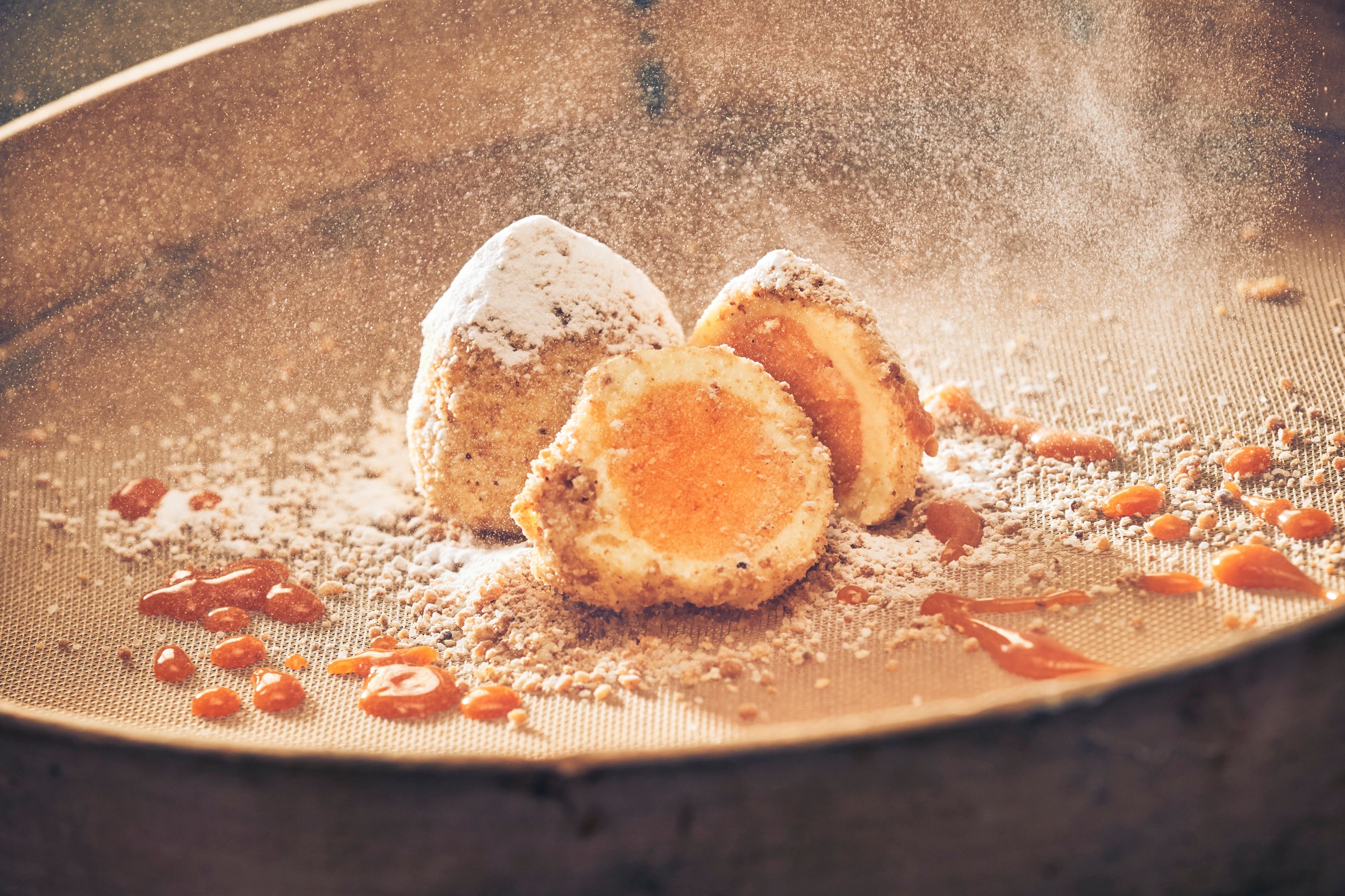 Iced apricot dumplings with powdered sugar and apricot sauce on a sieve.