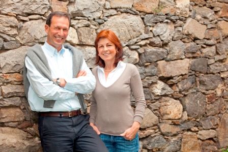 A man and a woman stand smiling in front of a stone wall.