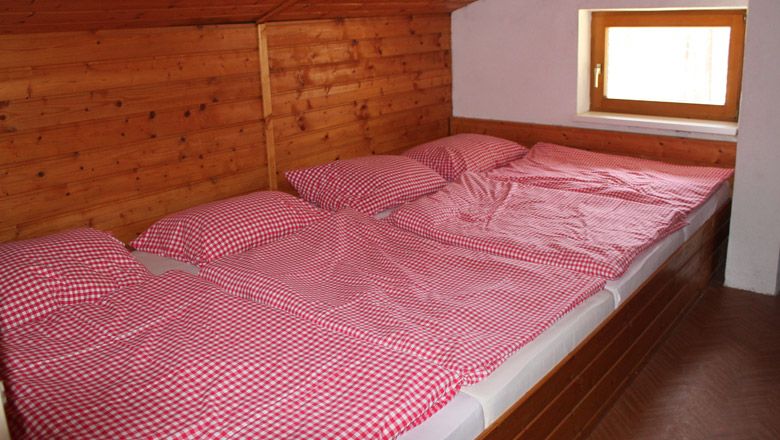 Three beds with red and white checked comforter covers in a wood-paneled room.