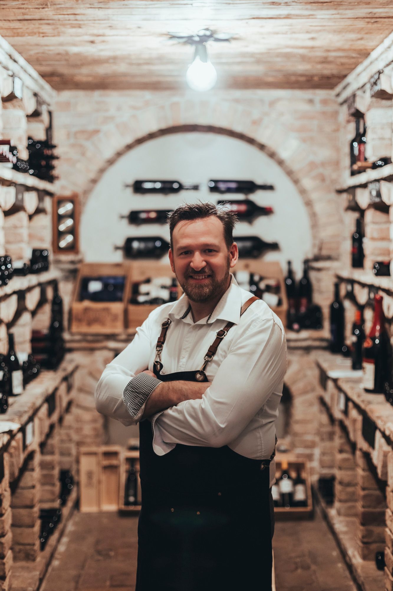 A man in a wine cellar with shelves full of wine bottles.