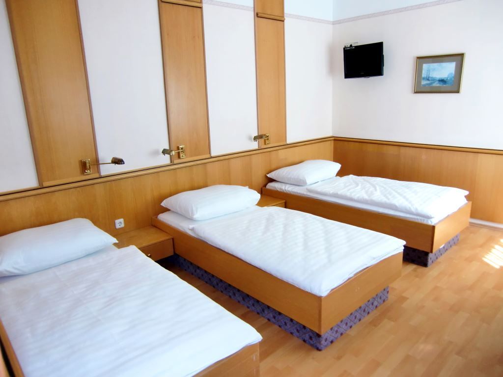 Triple room with three single beds, wooden walls, TV and picture on the wall.