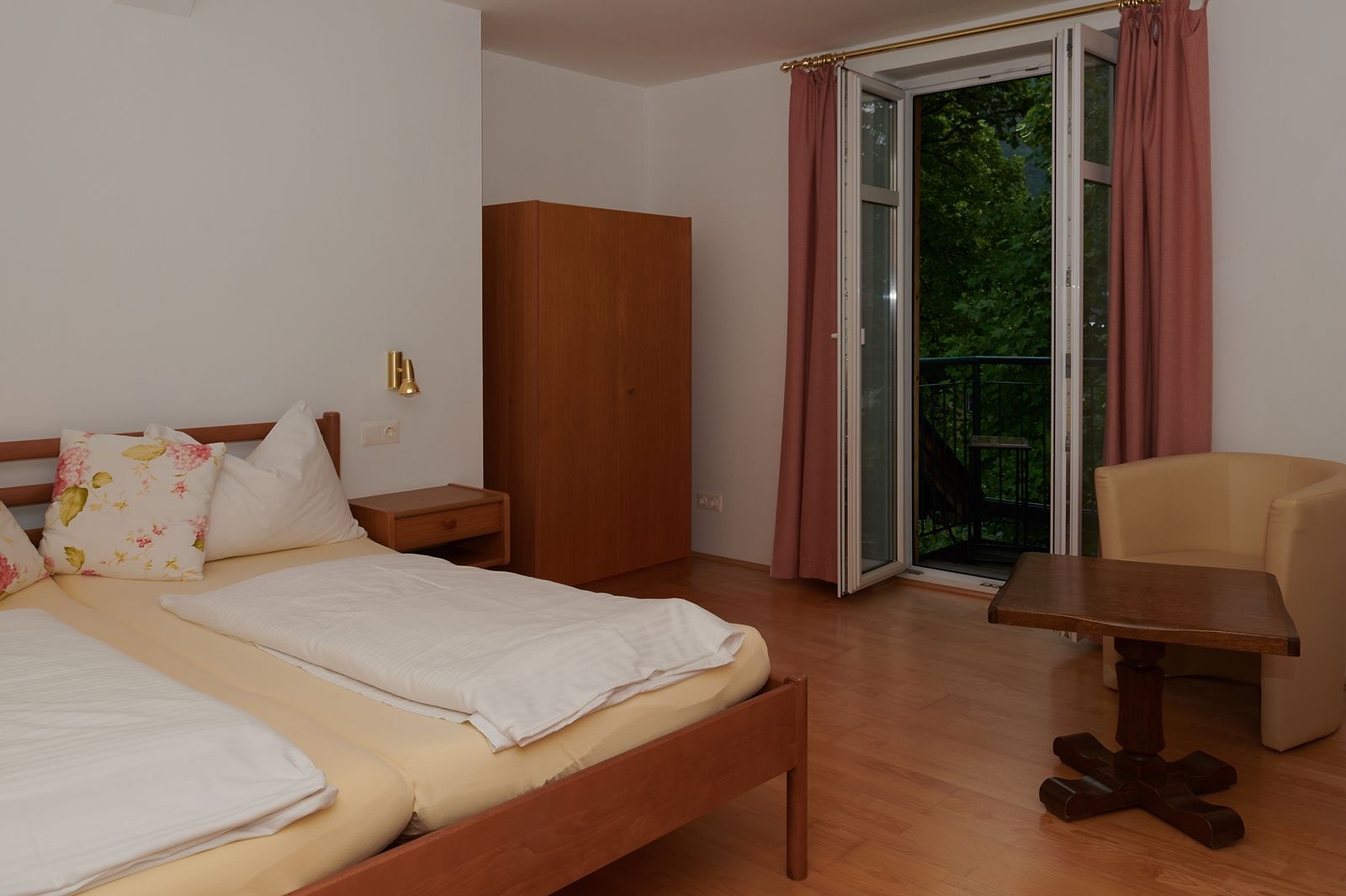 Bedroom with double bed, wardrobe, table and chair, window with curtains.
