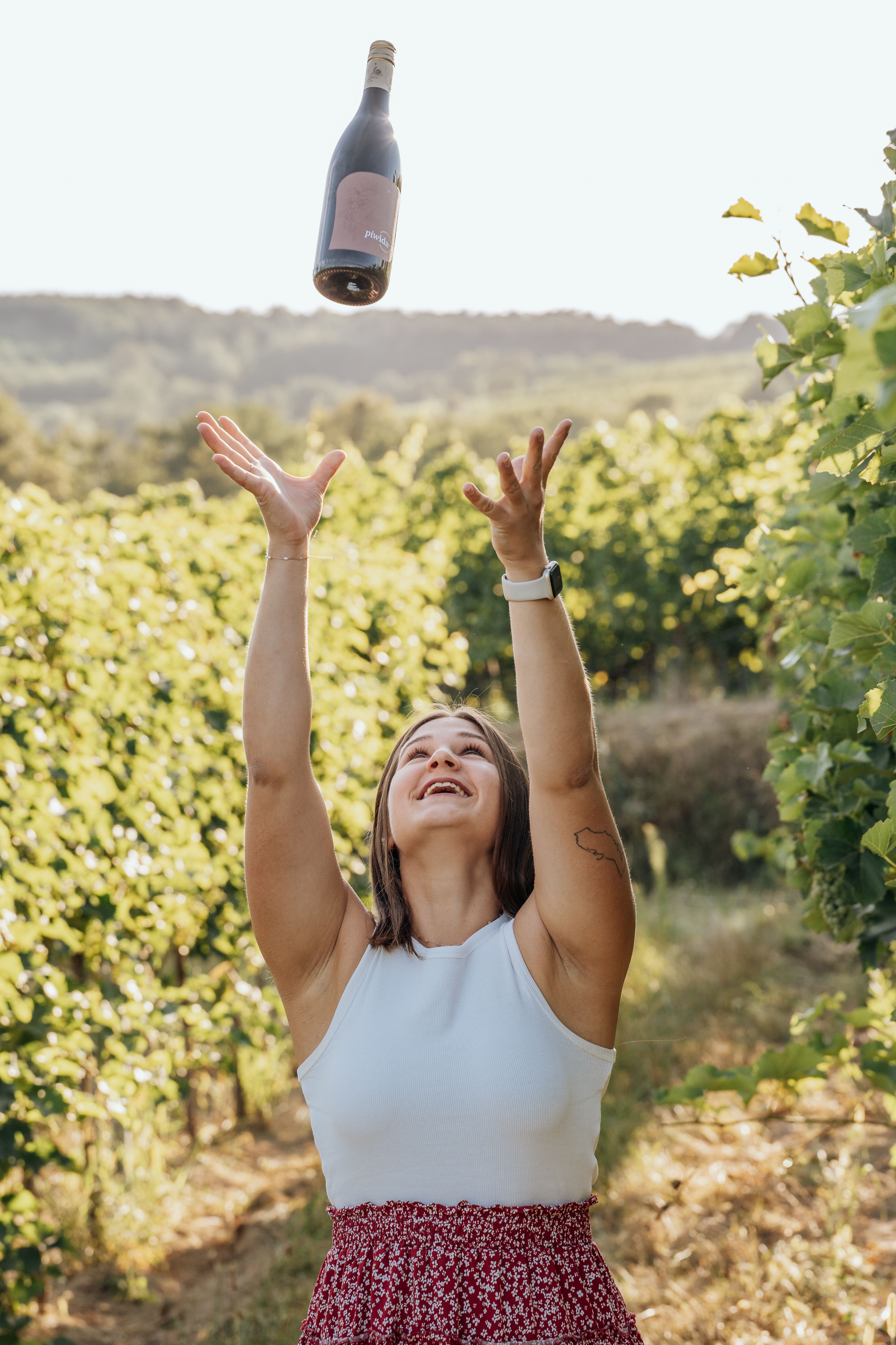 Woman throws wine bottle into the air in a vineyard.