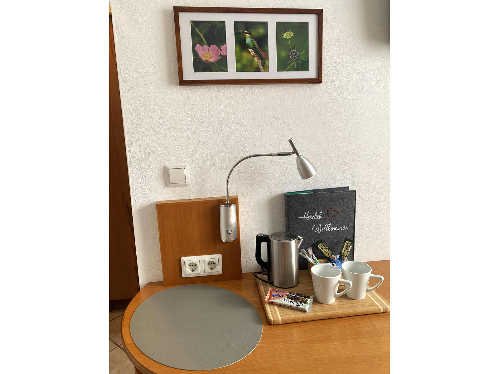 A table with a kettle, two cups, snacks and a welcome booklet. Three nature photos hang on the wall.