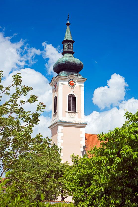 Tower of a church with clock and green roof in front of a blue sky.