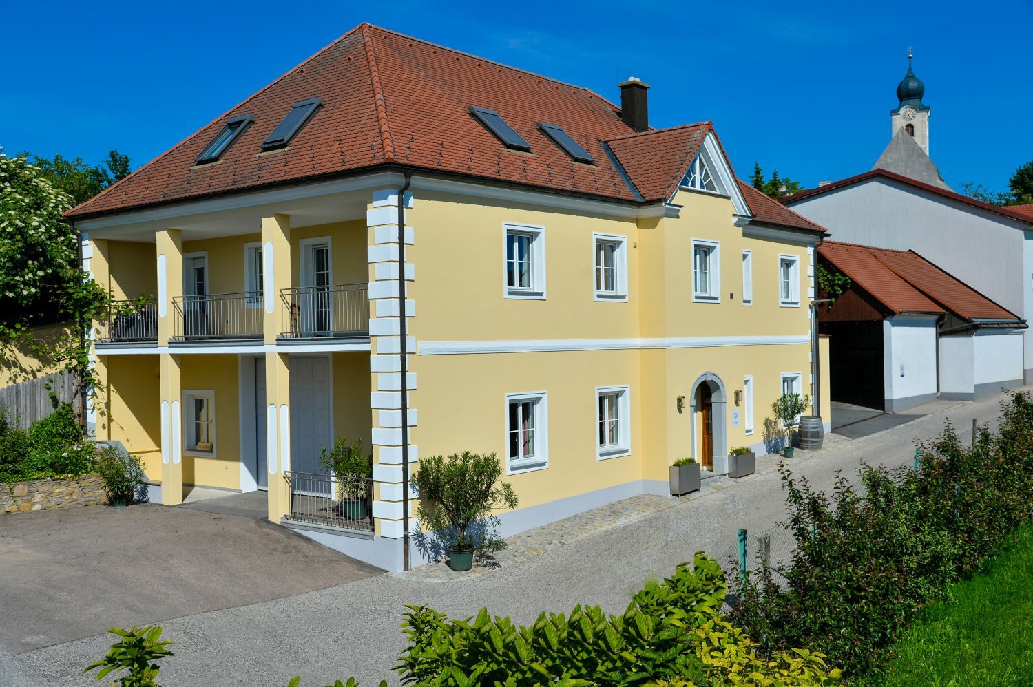 Yellow two-story house with a red roof and balcony, next to it a church with an onion dome.