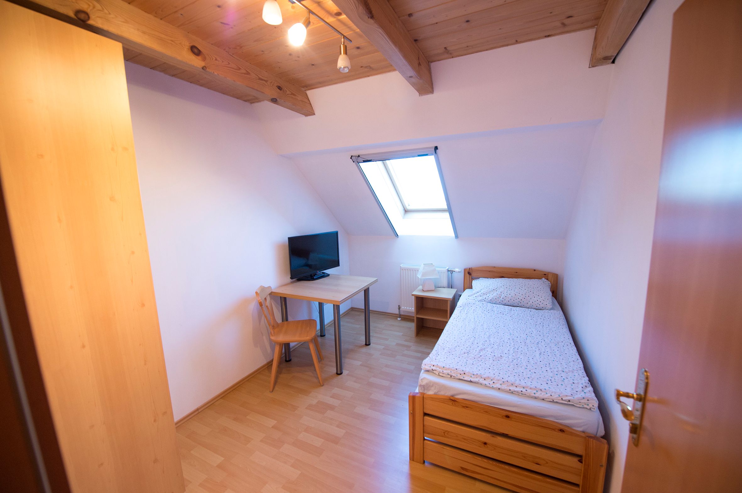 Room with sloping ceiling and a single bed. Behind it a table with TV and wardrobe.