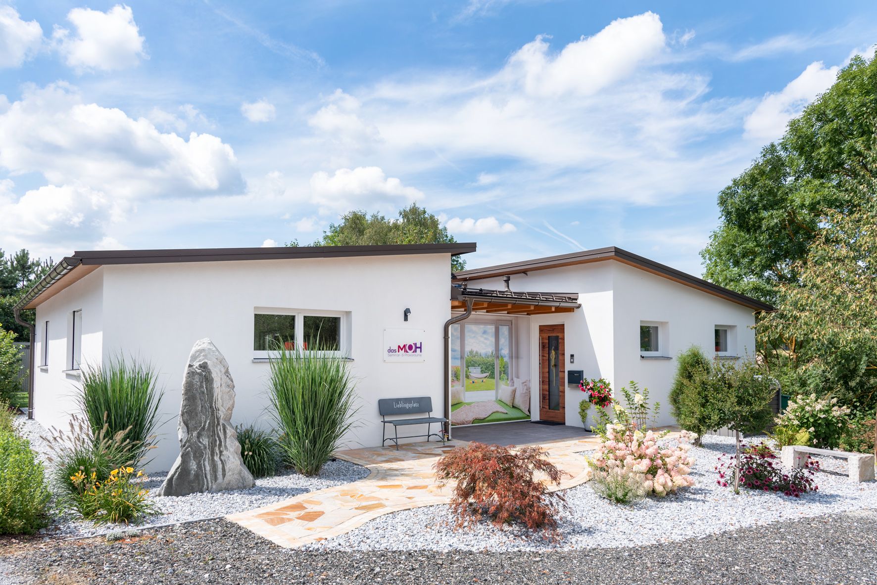 Modern, white building with garden and gravel path, blue sky in the background.