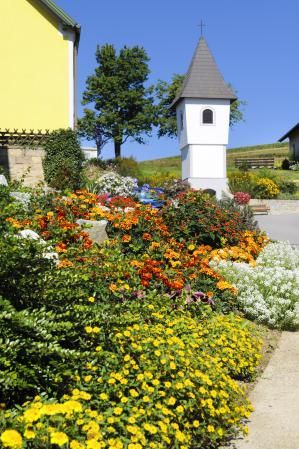 A blooming garden with colorful flowers in front of a small, white chapel building.