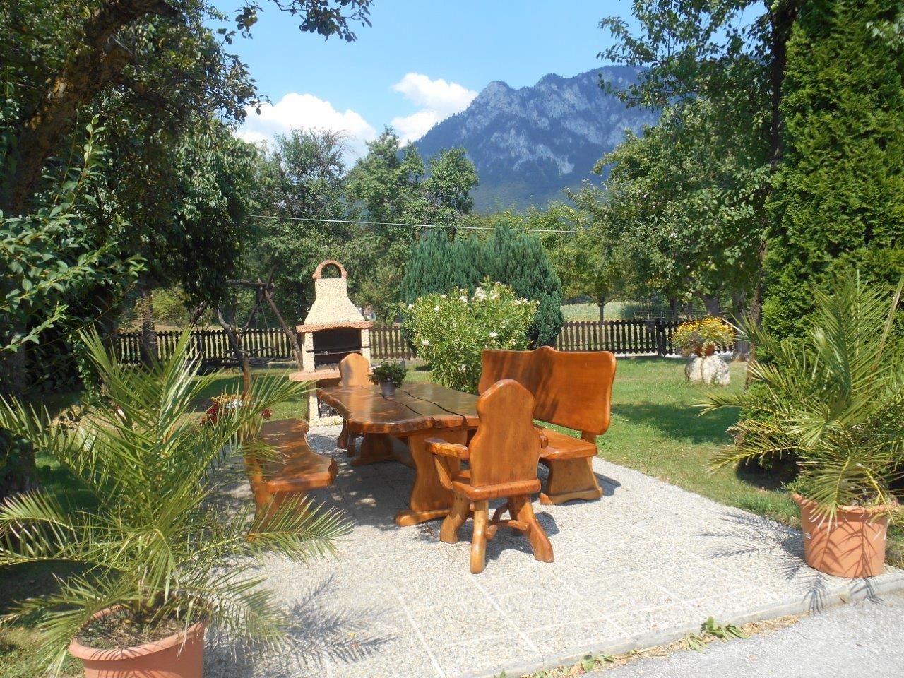 Garden area with wooden furniture and barbecue against a mountain backdrop.