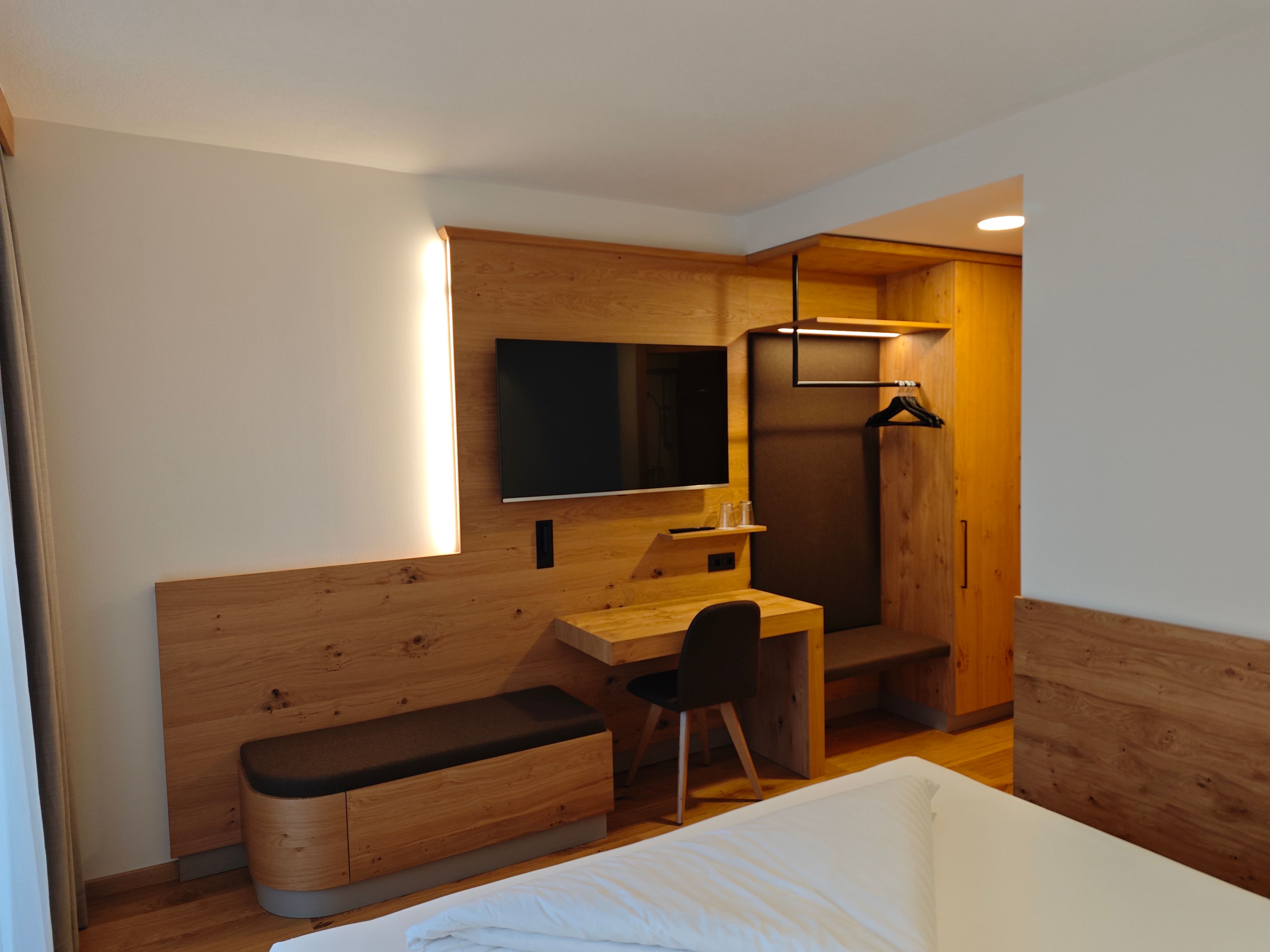 A modern hotel room with wooden furniture, a desk, a TV, and a closet.