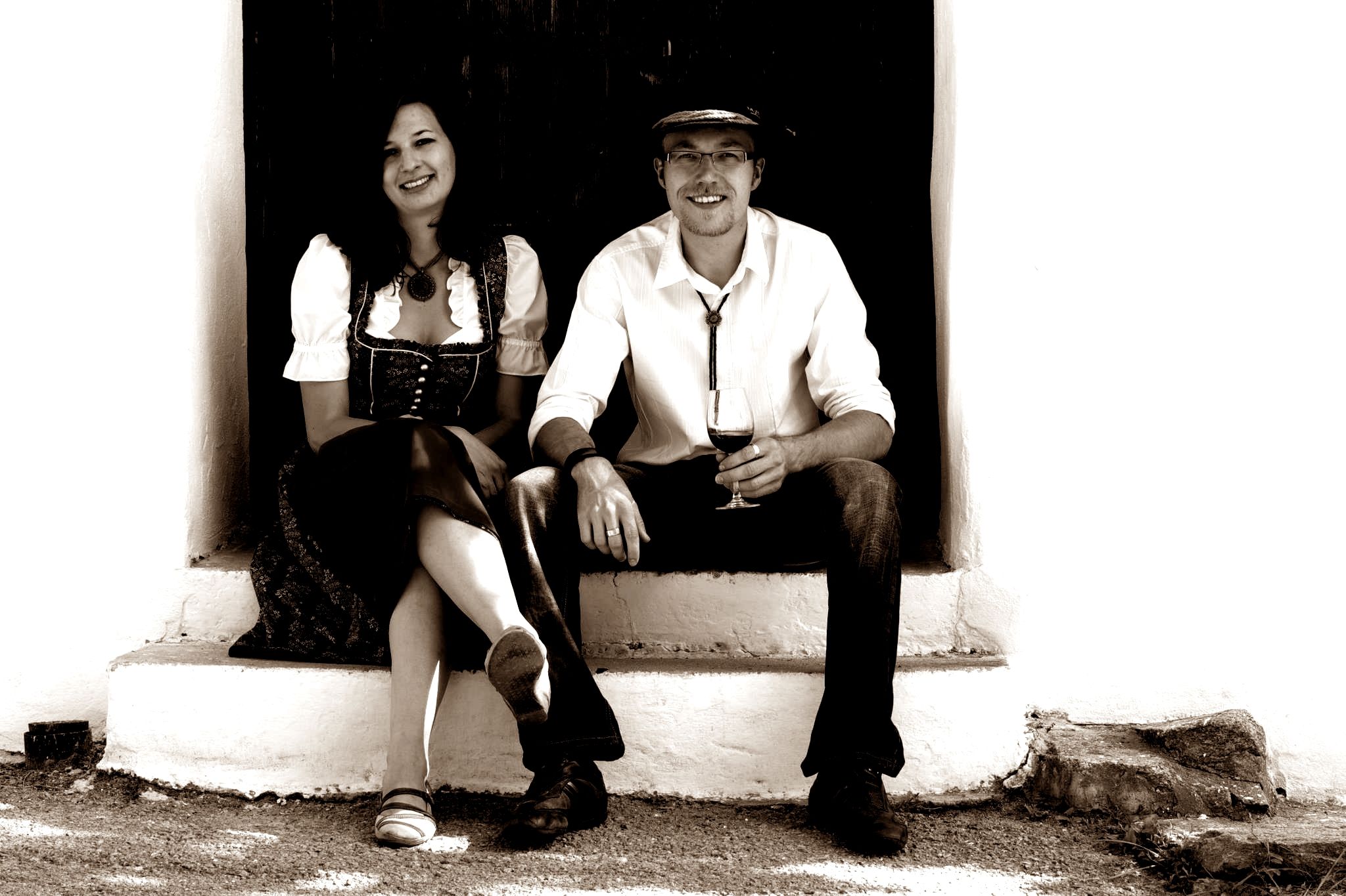 A man and a woman are sitting on a staircase, the man is holding a wine glass.