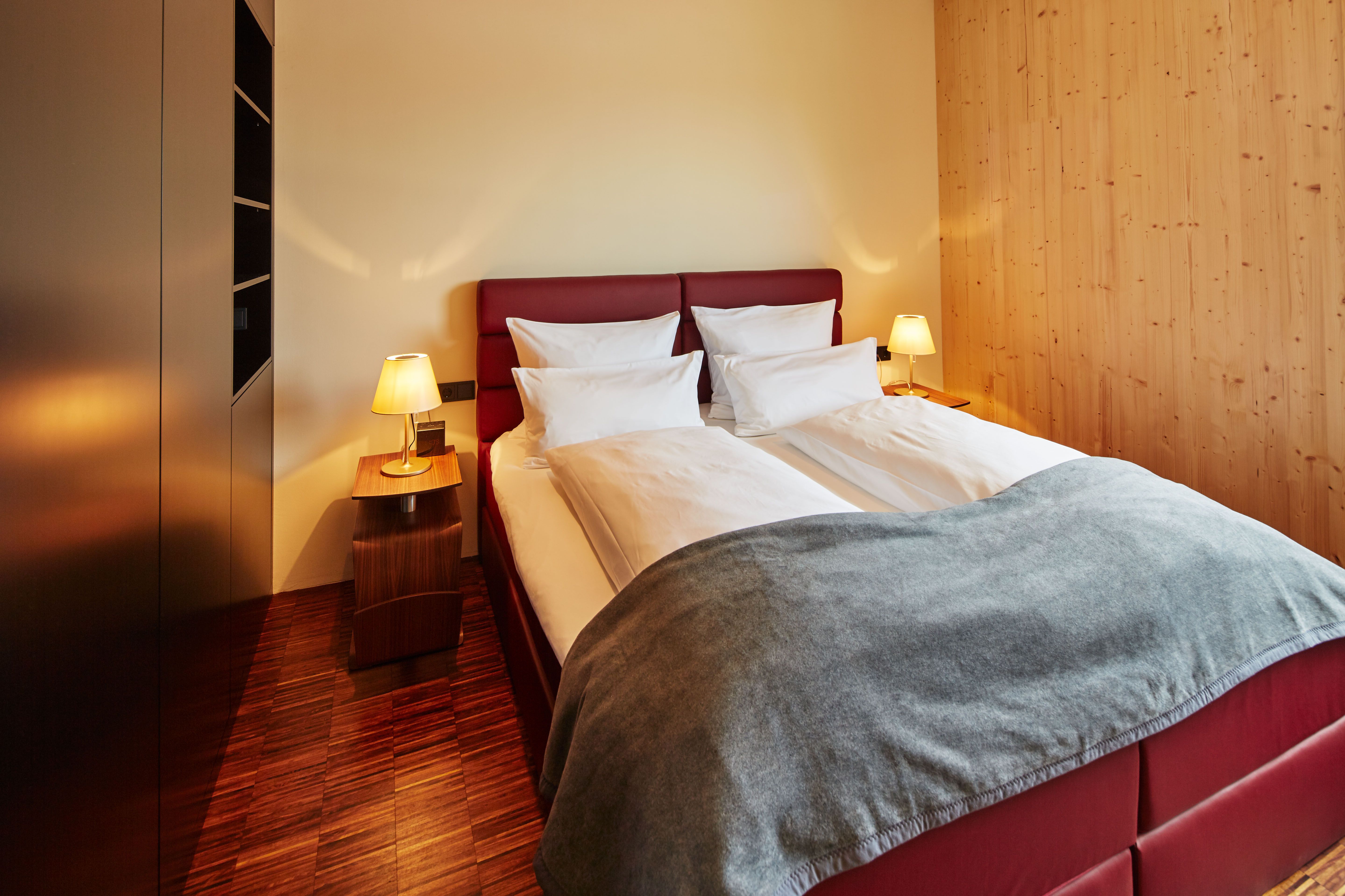 A cozy bedroom with a double bed, red headboard, two bedside tables with lamps and wooden walls.