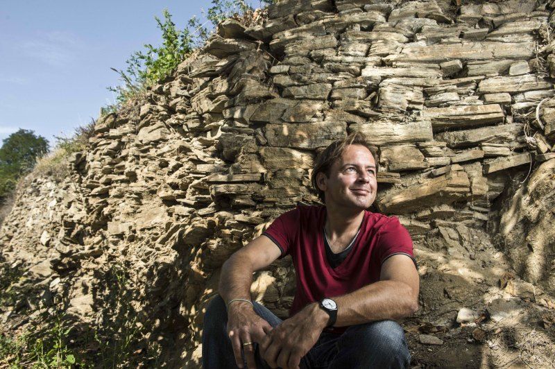 Man in red T-shirt sitting in front of a rock face.