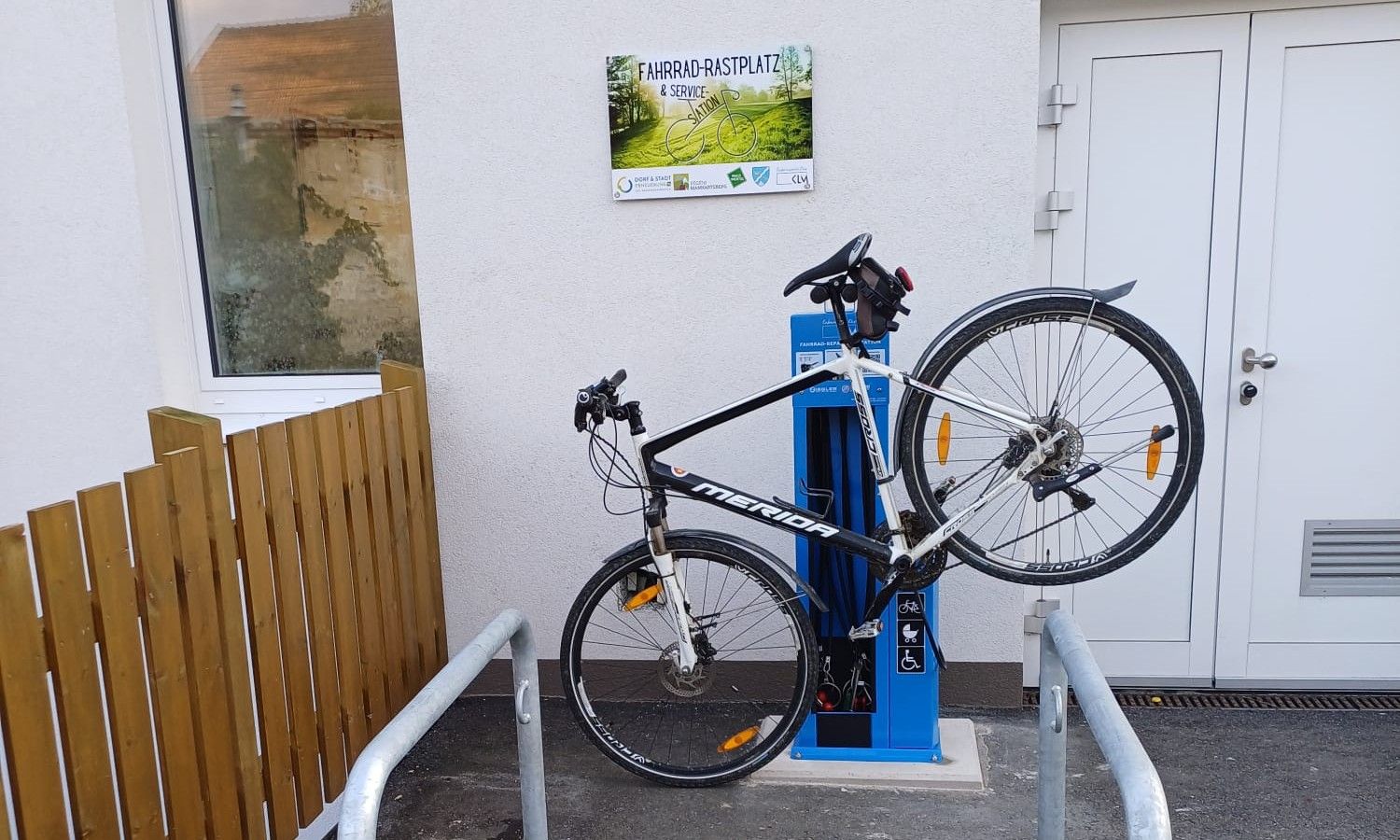 Bicycle attached to a blue service station, next to a building with a 'Bicycle Rest Area & Service Station' sign.