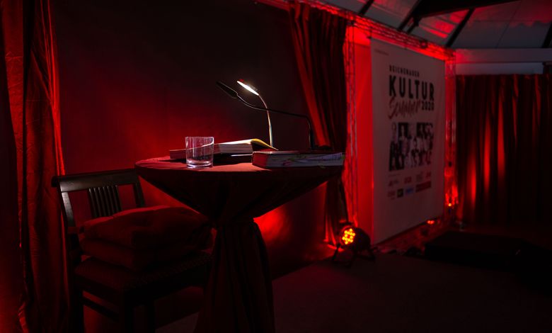 An illuminated table with microphone and glass in front of a red curtain.