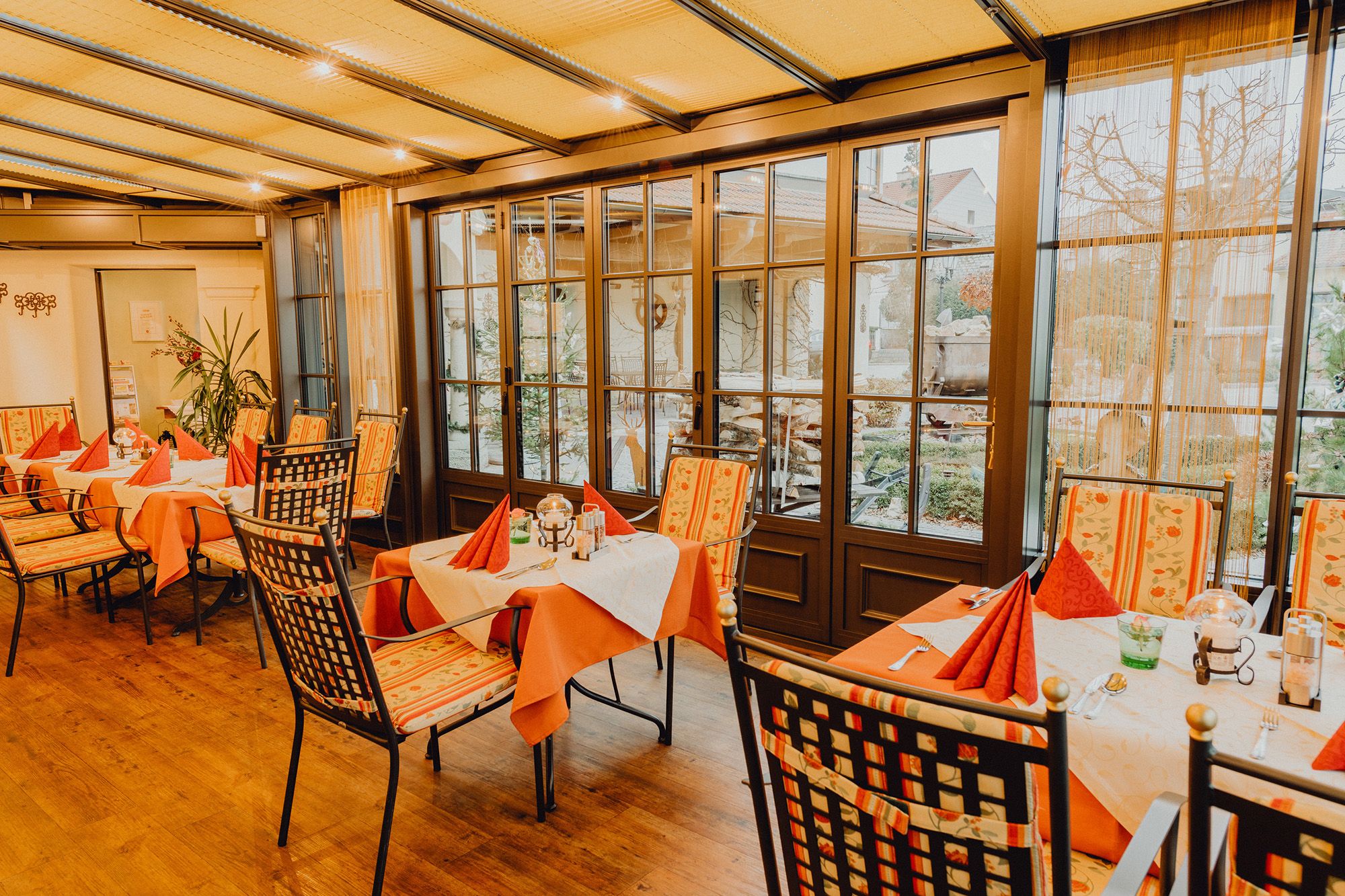 A cozy winter garden with covered tables and chairs, surrounded by large windows with a view outside.