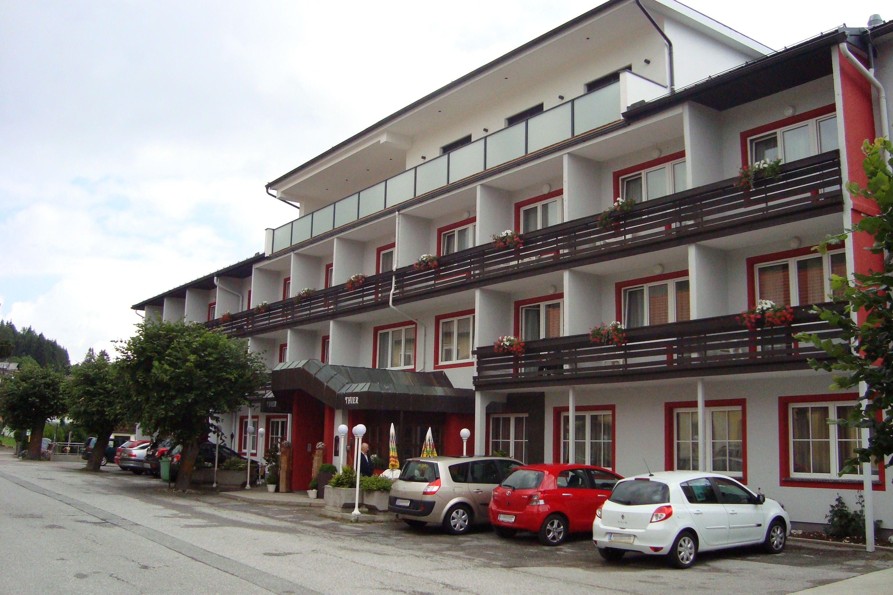 Exterior view of Hotel Thier with parked cars and balconies with flowers.