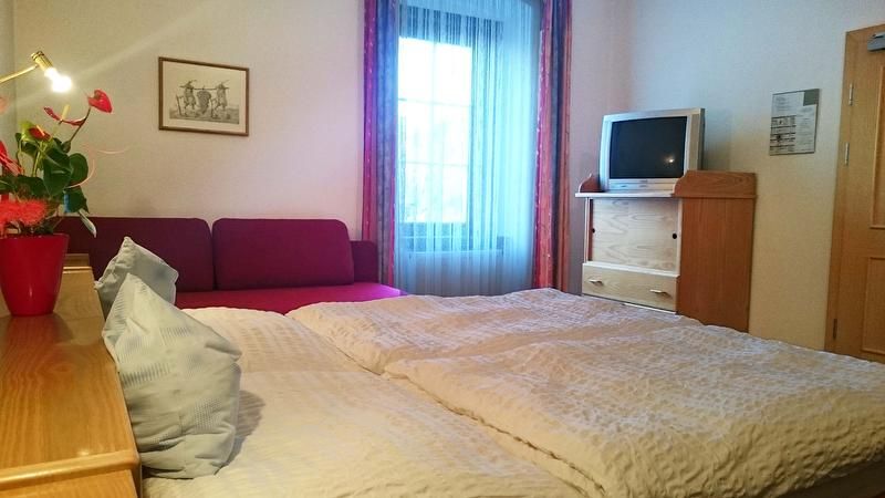 A cozy double room with bed, sofa, TV and window.