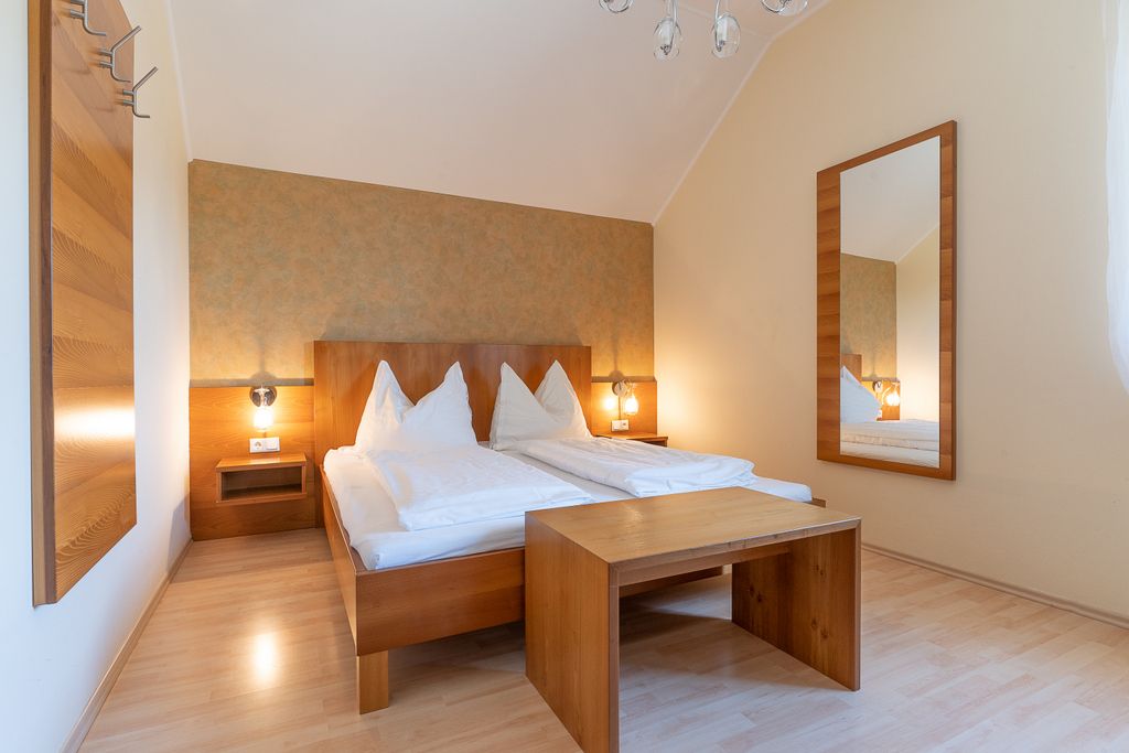 A simply furnished bedroom with double bed, wooden furniture and large mirror.
