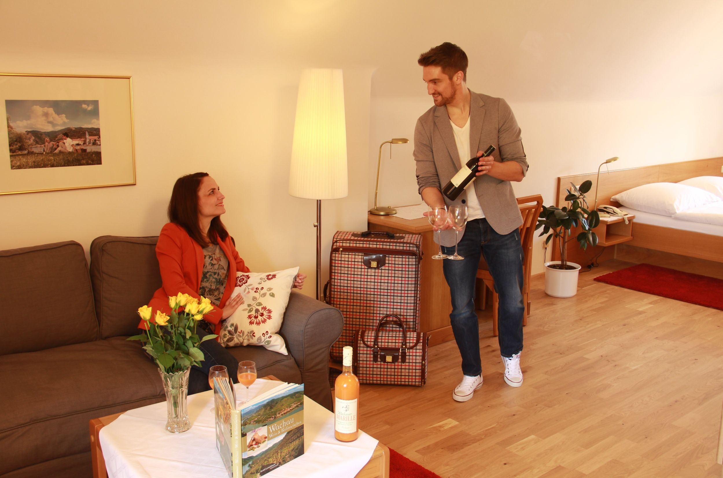 A man pours wine for a woman in a cozy hotel room.