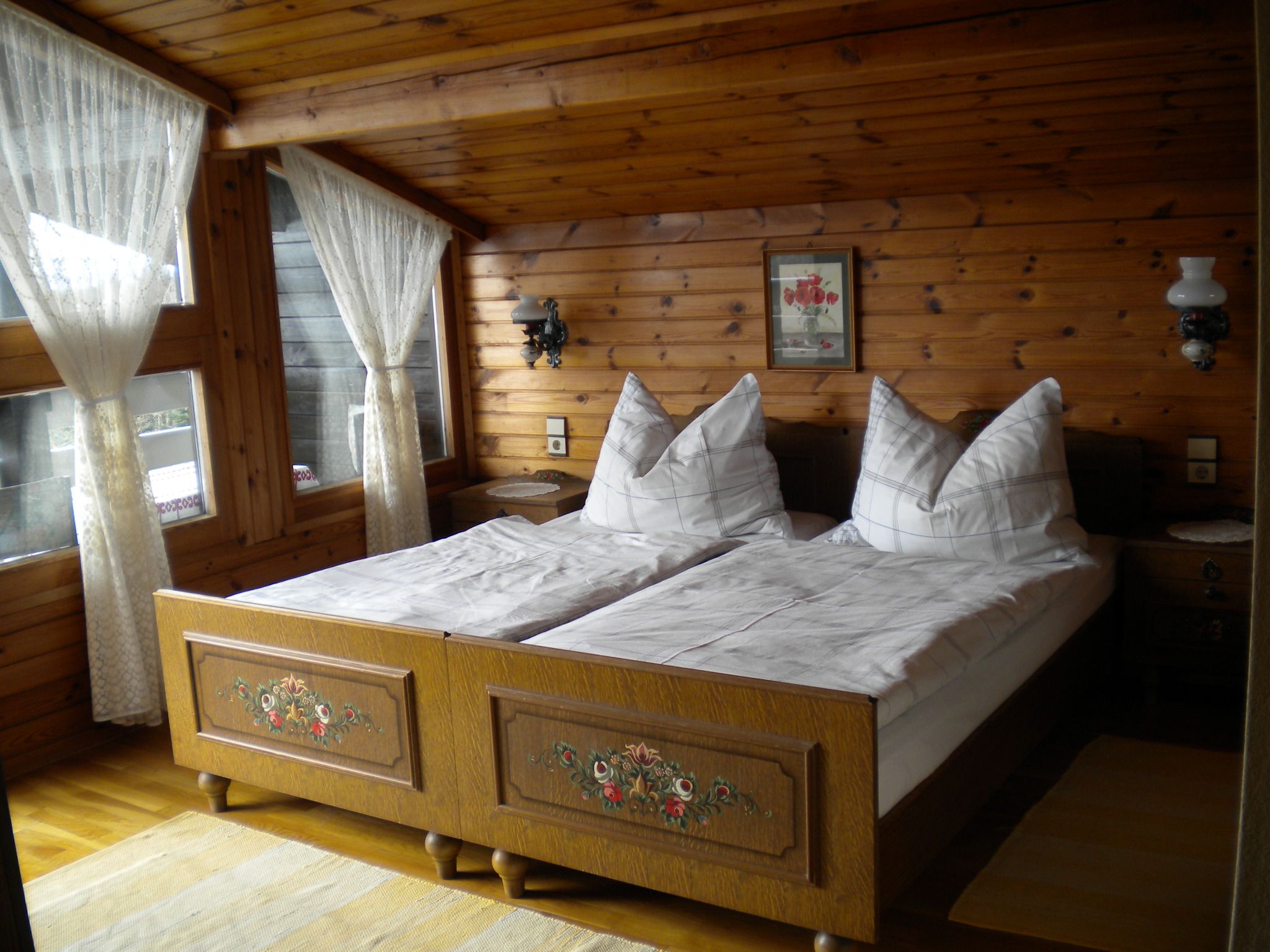 Cozy bedroom with wooden walls, double bed and lace curtains.
