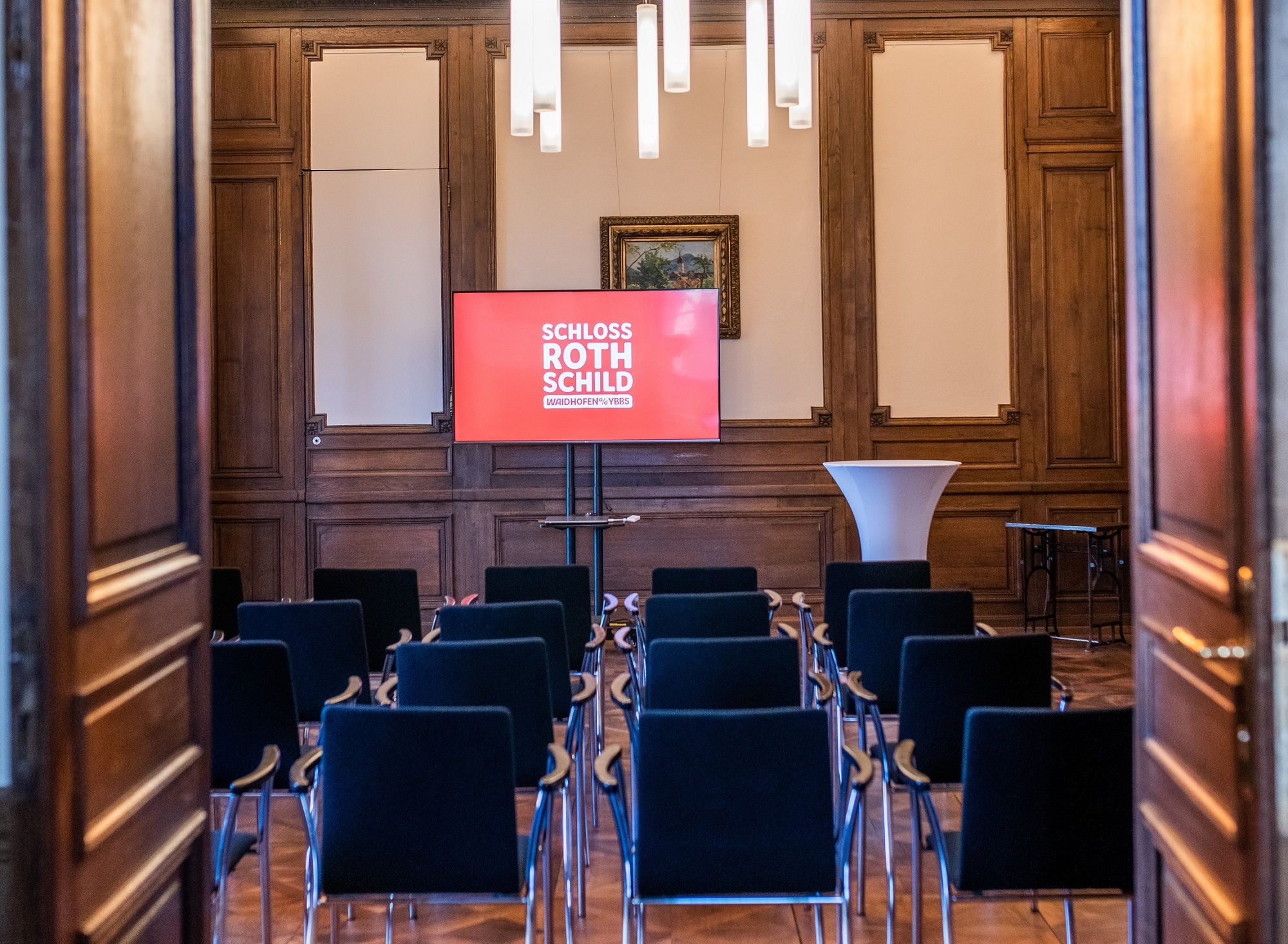 A seminar room in Schloss Rothschild with rows of chairs, a screen and a high table.