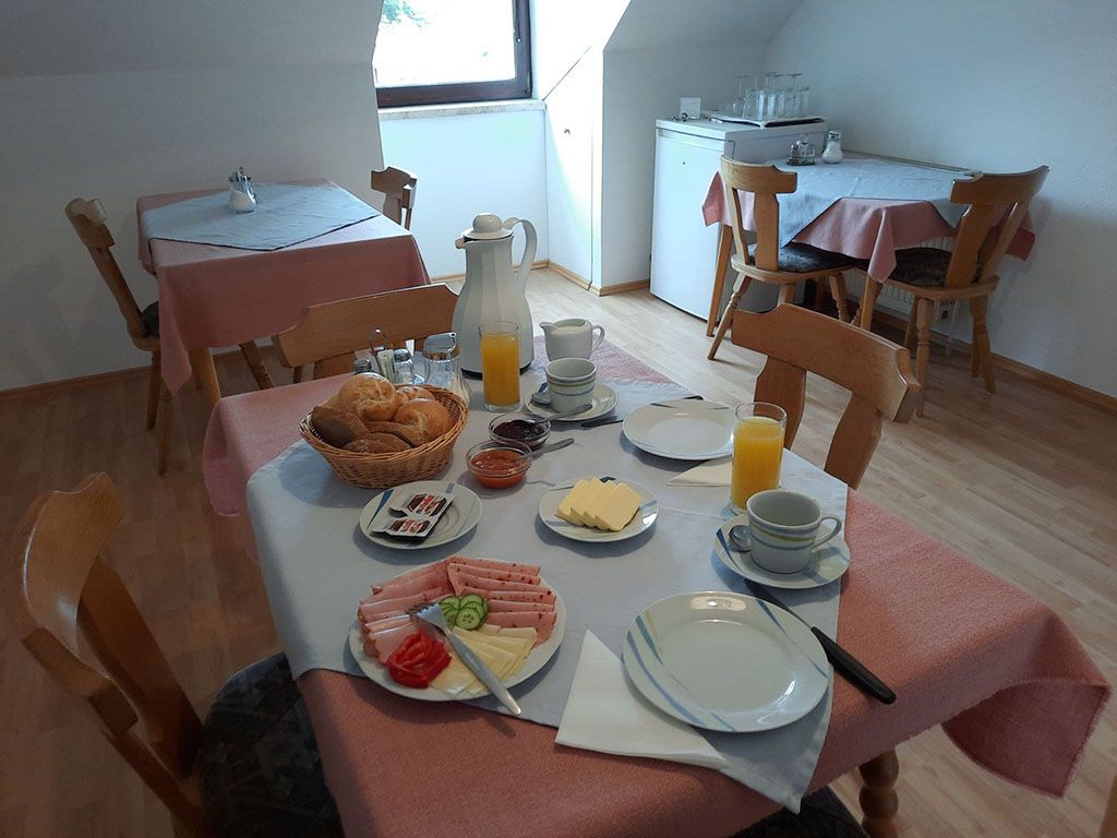 A laid breakfast table with bread rolls, cold cuts, cheese and orange juice in a cozy room.