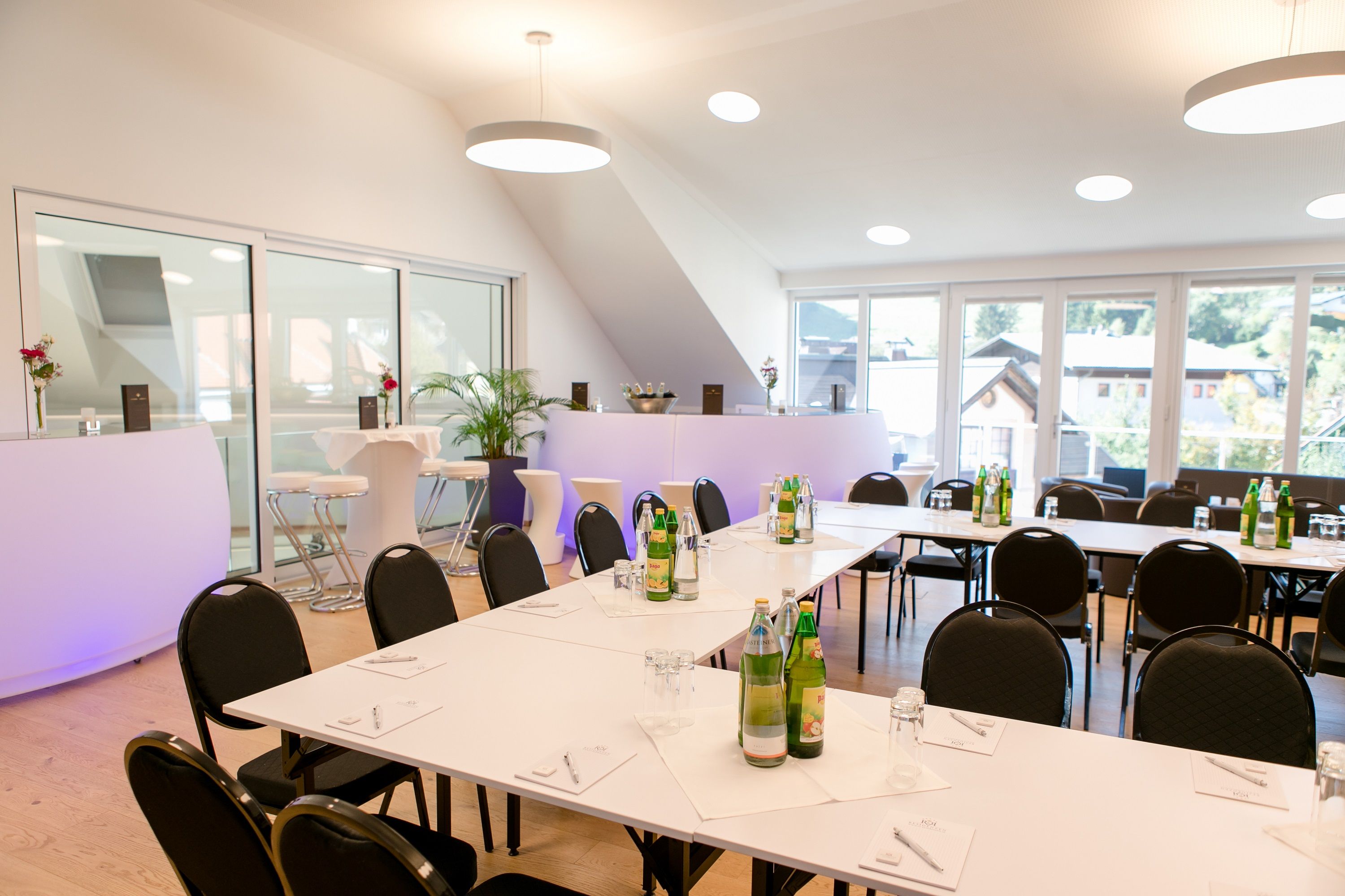 Modern seminar room with white tables, chairs and drinks, large windows with a view outside.