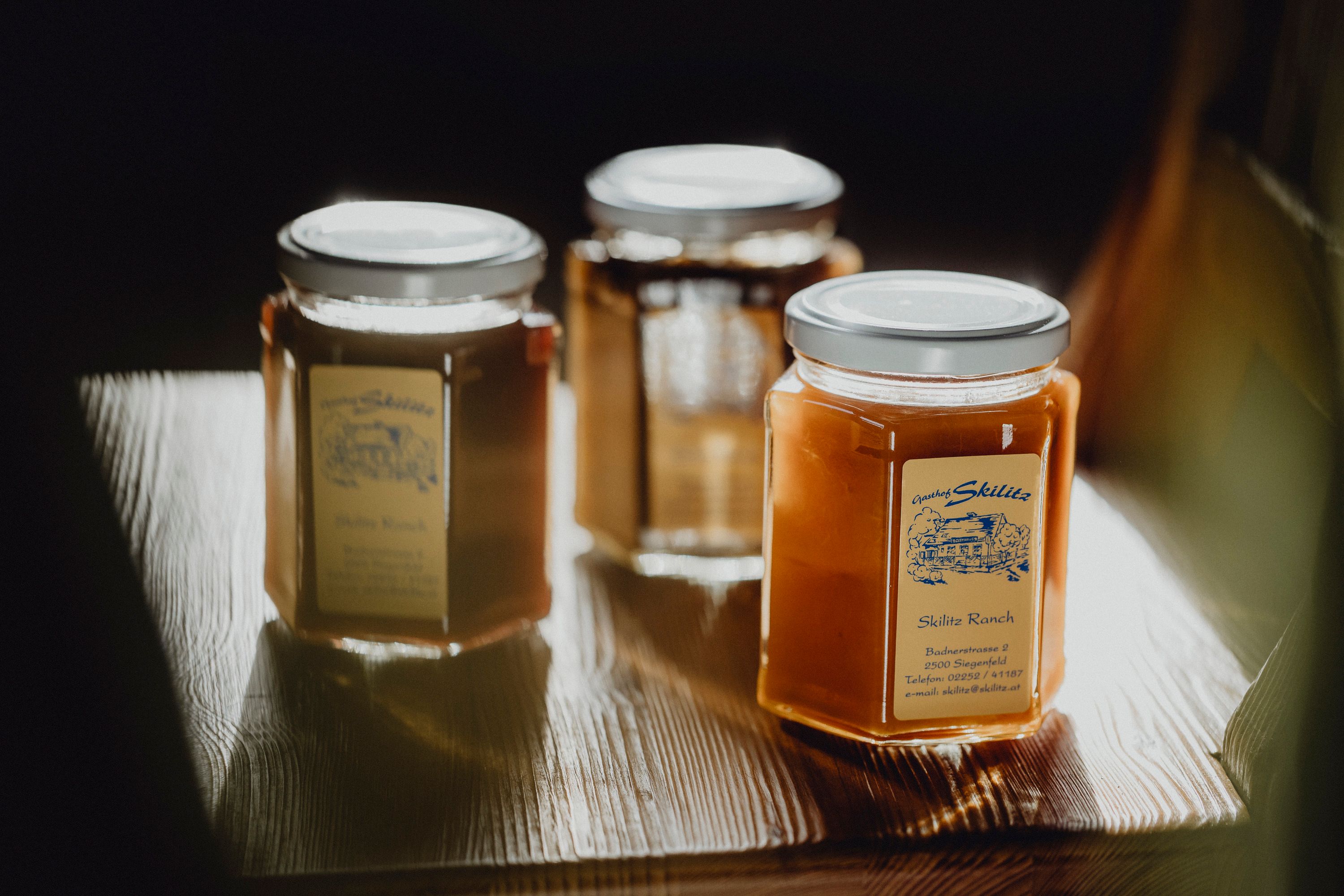 Three jars of honey on a wooden table.