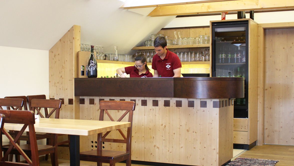 Two people behind a wooden bar in a rustic room.