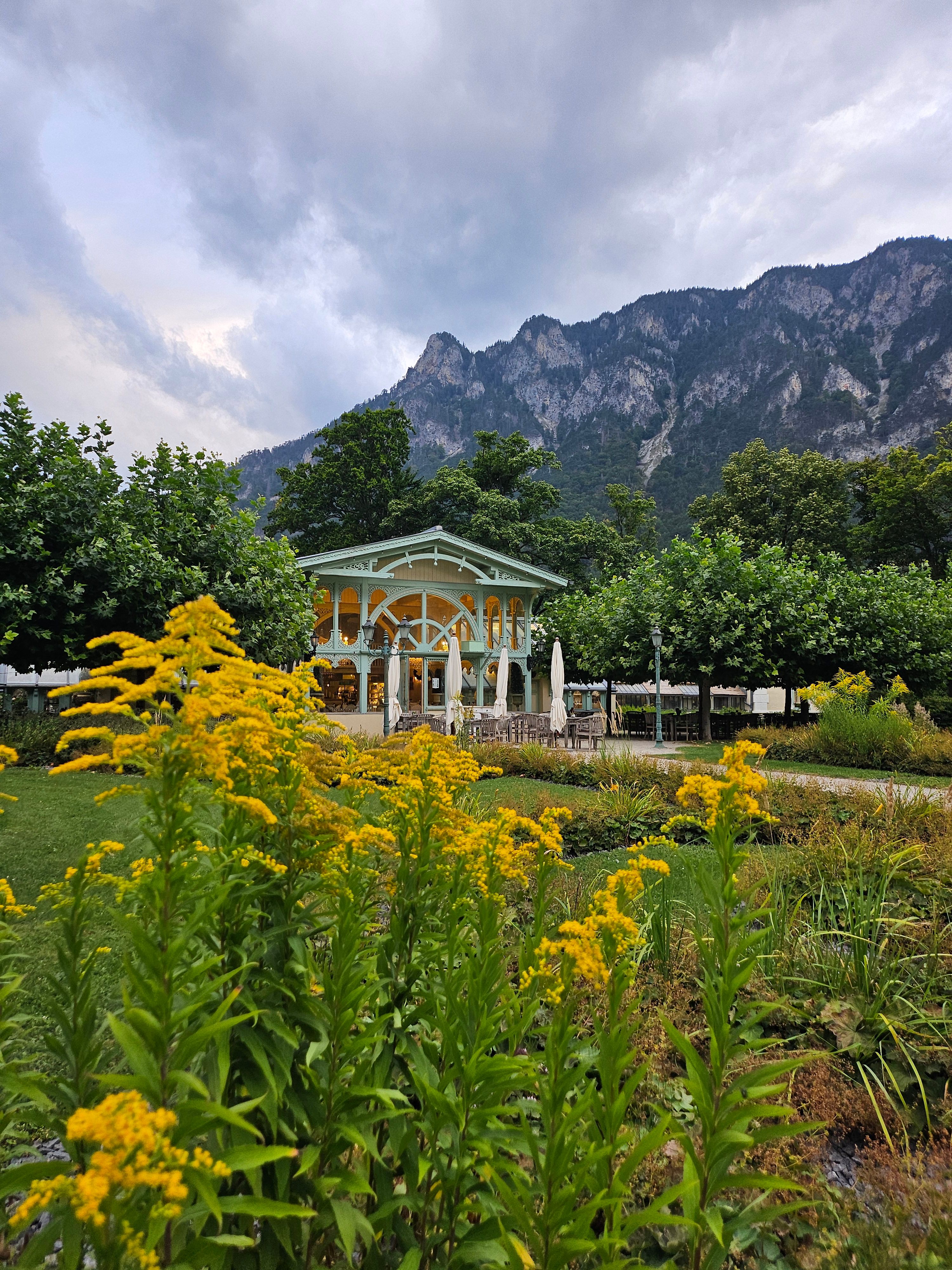 A pavilion in a garden with yellow flowers in the foreground and mountains in the background.