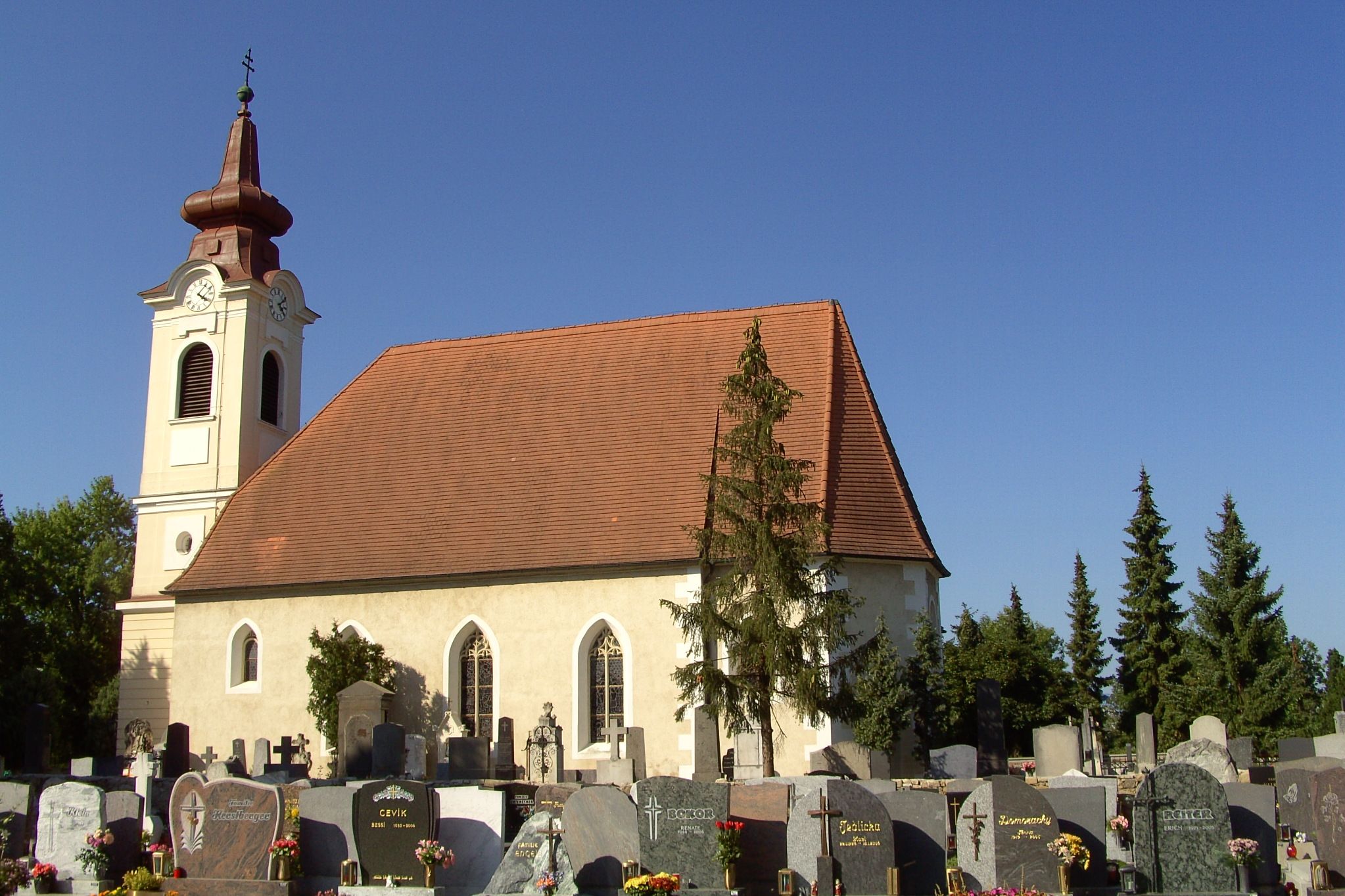 Exterior view of a church with a cemetery in the foreground and a blue sky.